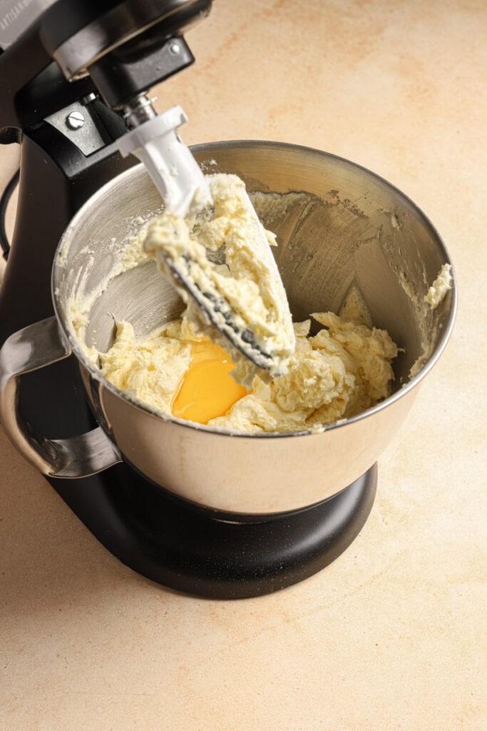A stand mixer with a bowl filled with creamed butter and sugar and an egg.