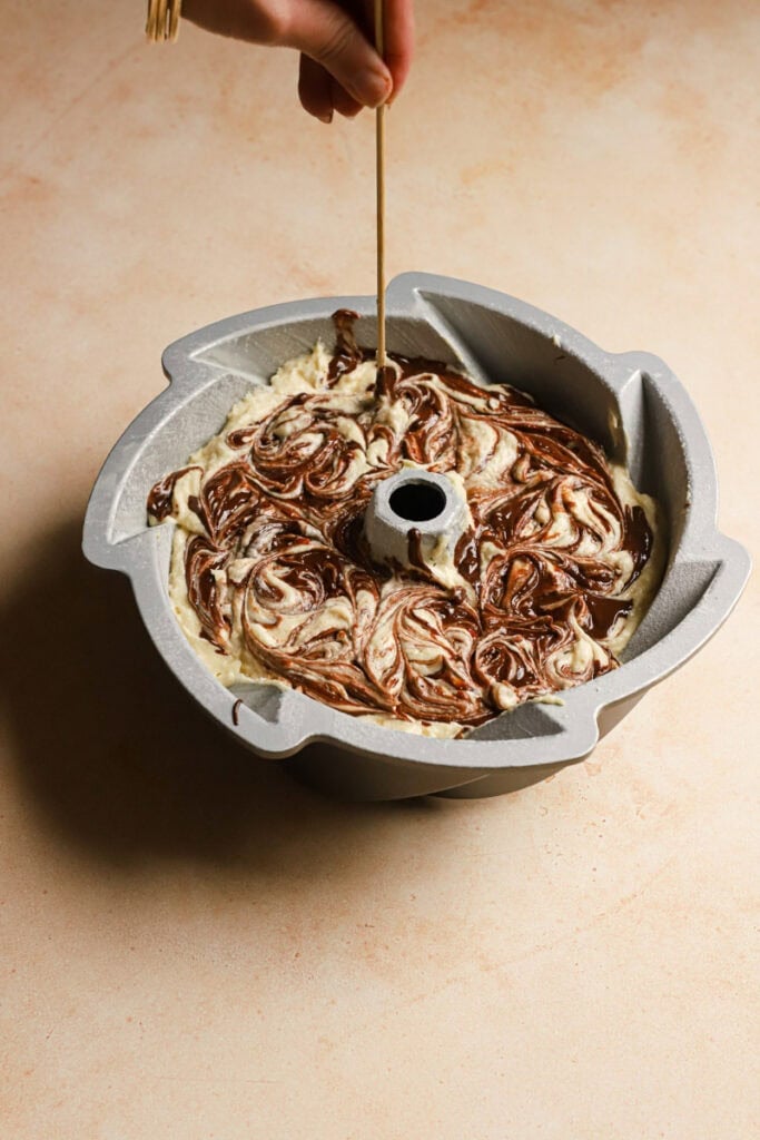swirling melted chocolate into a cake batter using a wooden skewer.