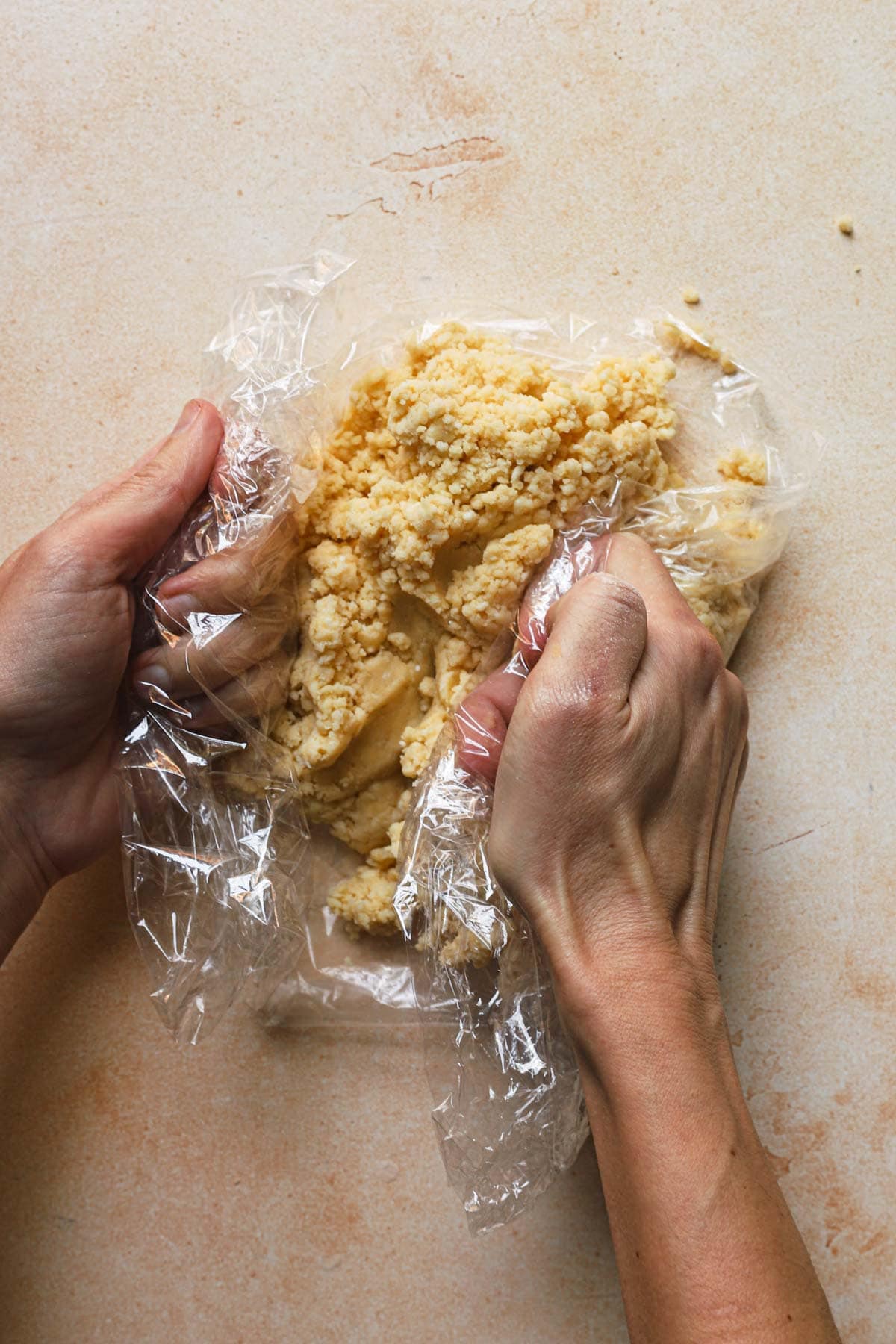 hands pressing dough suing plastic wrap.