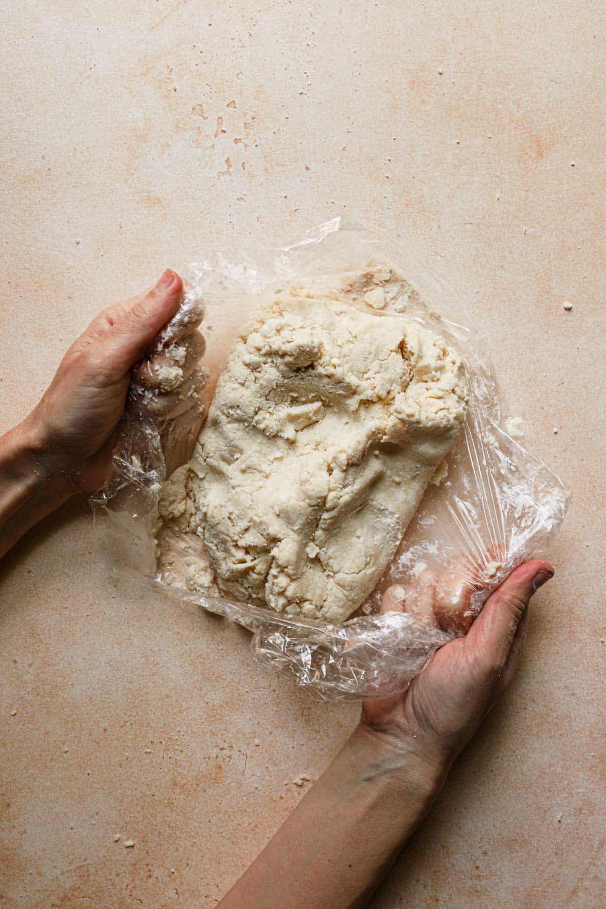 Hands holding plastic wrap to press dough