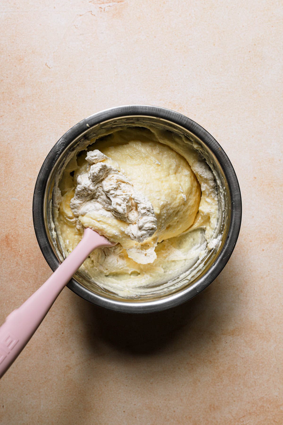 A rubber spatula folding ricotta cream into a pastry cream.