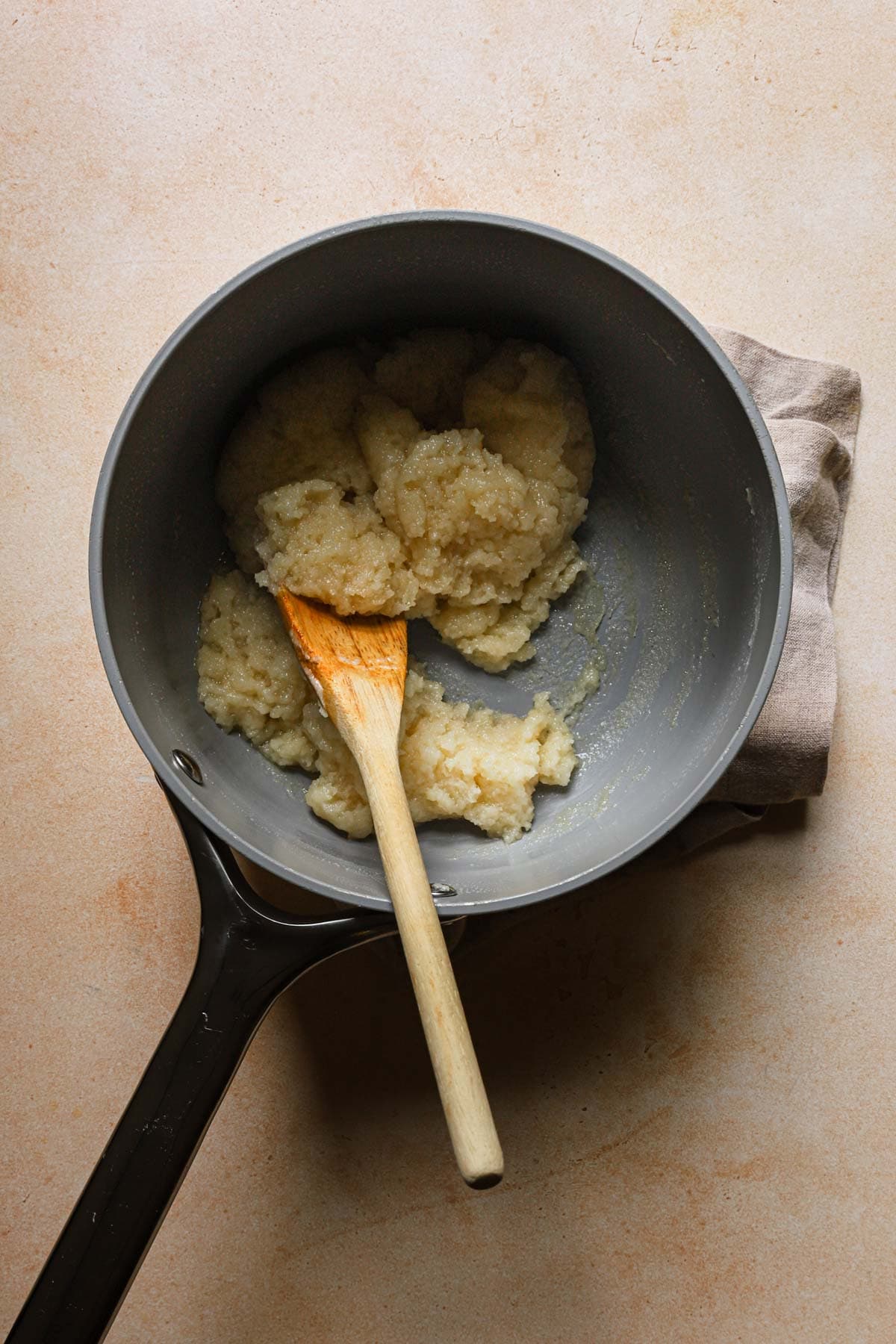A sauce pan with flour mixture for cream puffs and a wooden spoon.