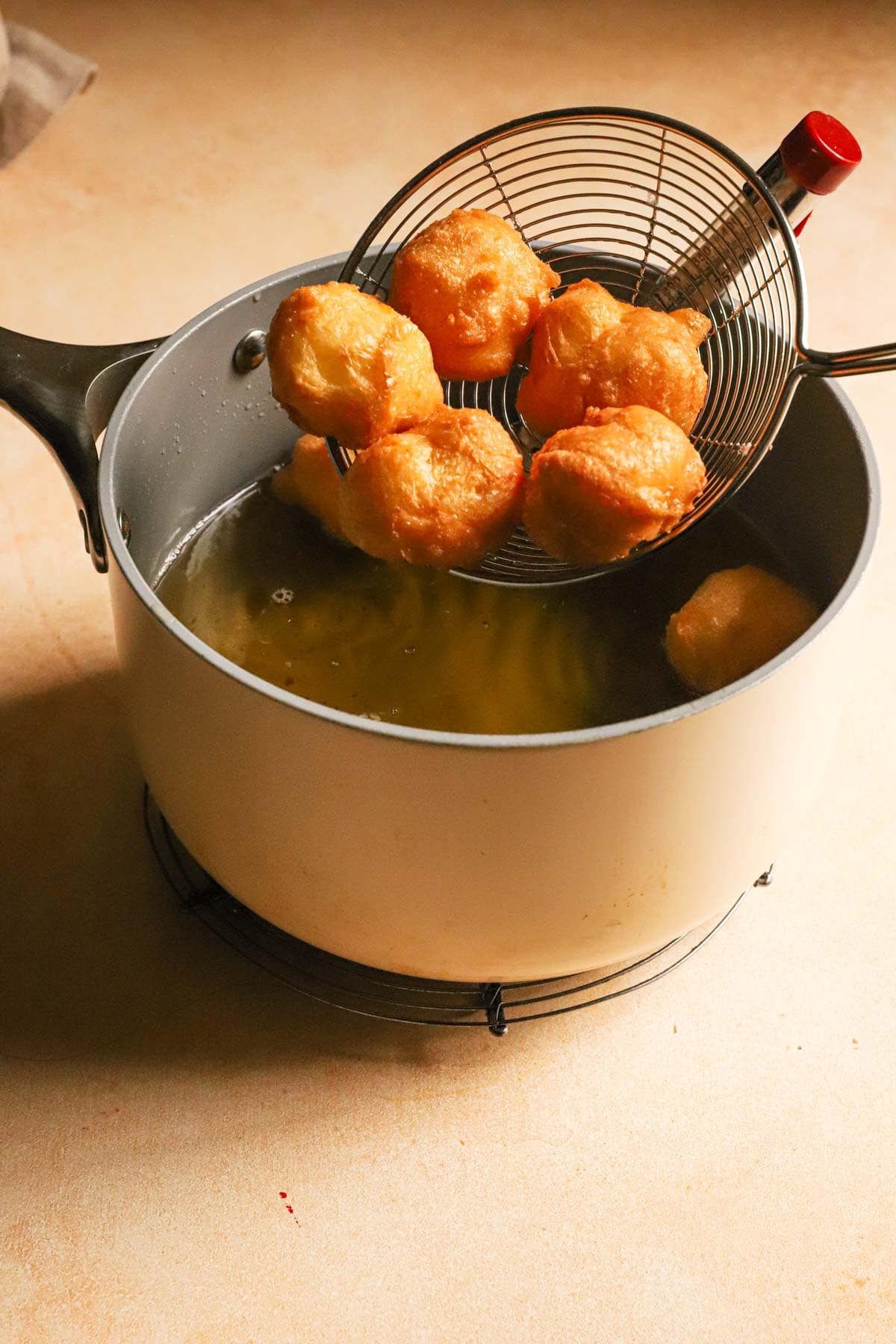 A slotted spoon removing fried italian cream puffs from hot oil.