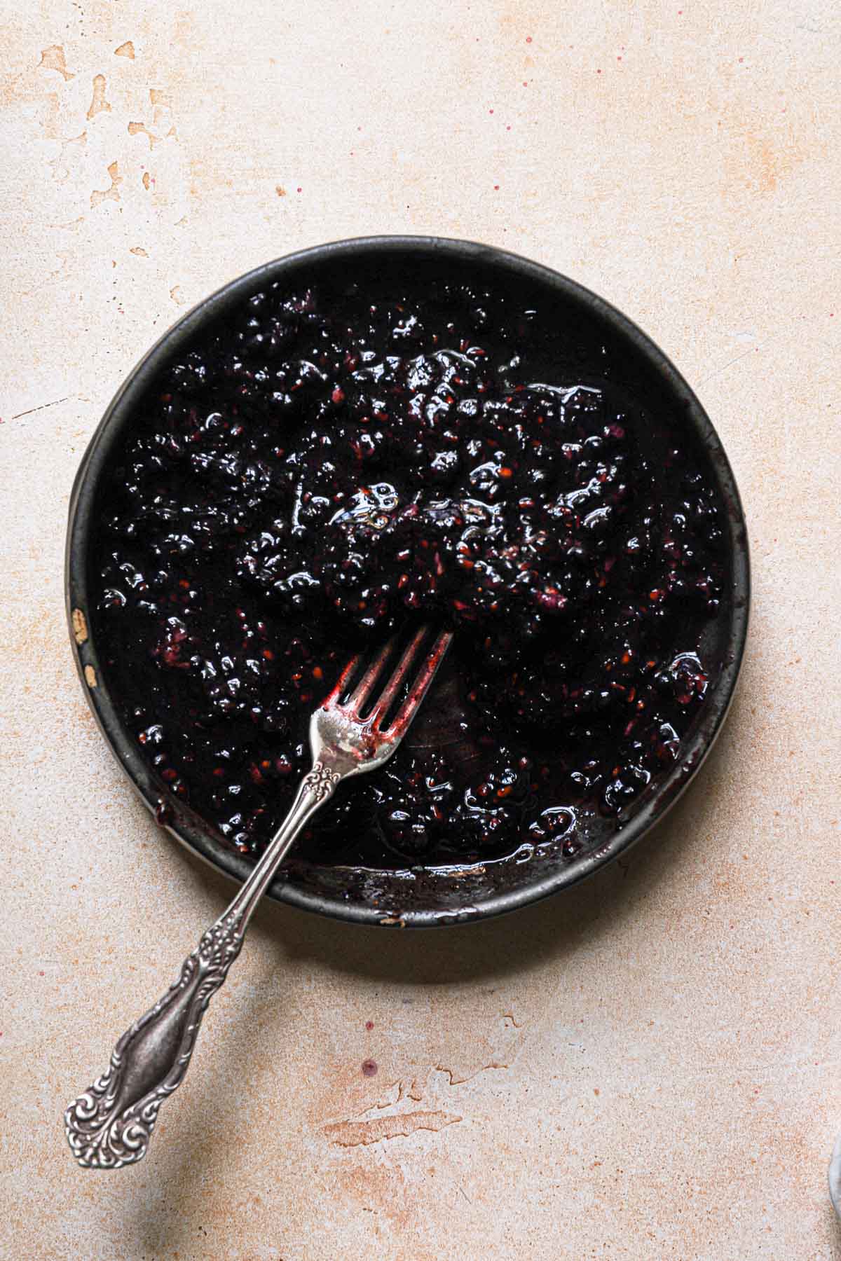 A bowl with mashed blackberries and a fork.