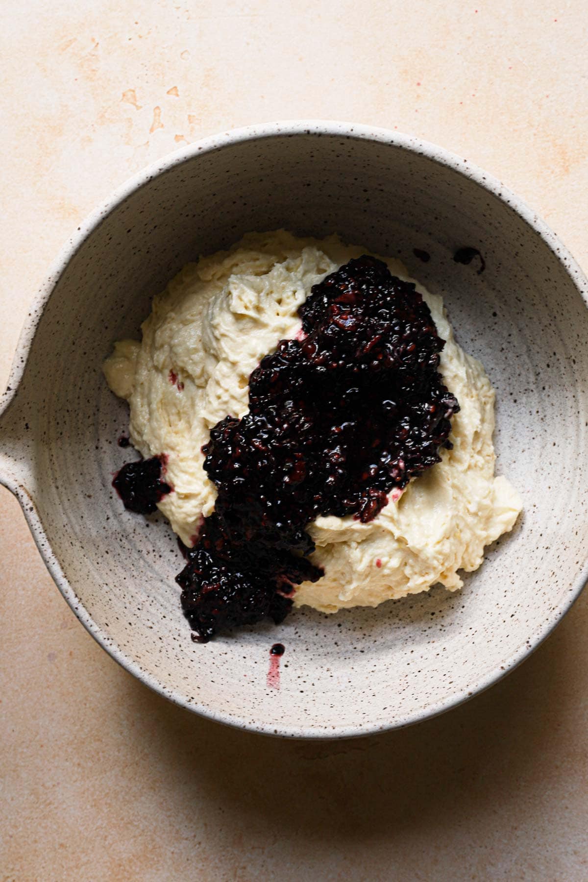 A bowl with cake batter topped with blackberry puree.