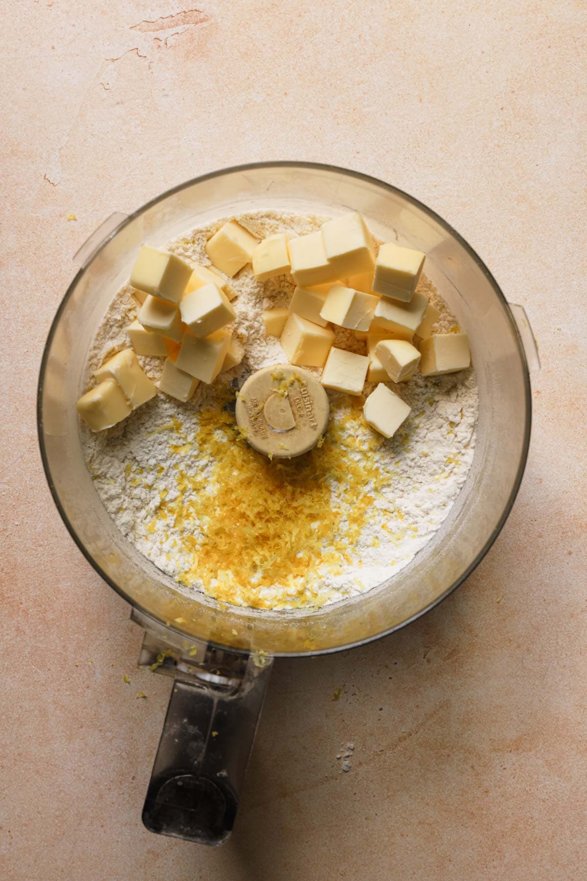 A food processor bowl with flour, lemon zest and butter.