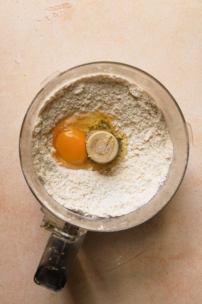 A food processor bowl with flour mixture and and egg.