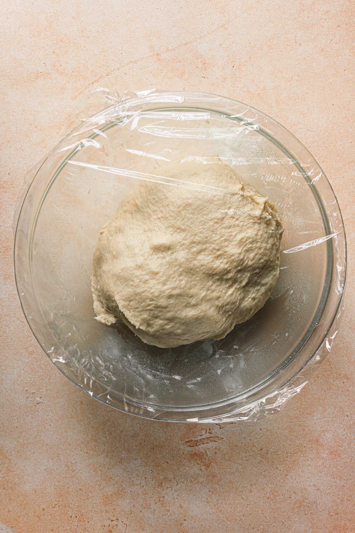 A bowl with dough covered with plastic wrap.