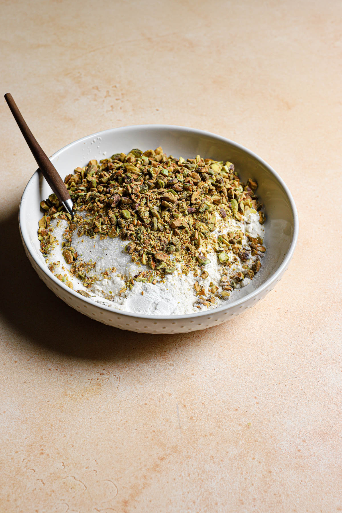 A bowl with flour mixture and chopped pistachio and a fork.