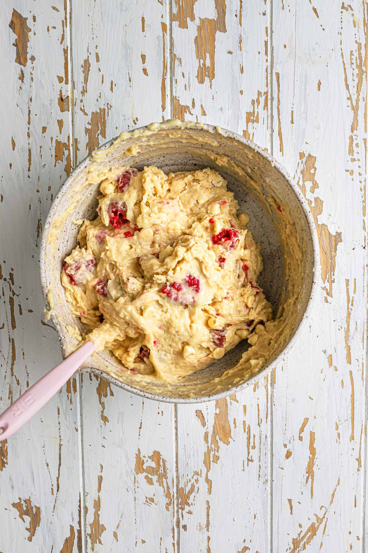 White chocolate raspberry muffin batter in a bowl with a spatula.