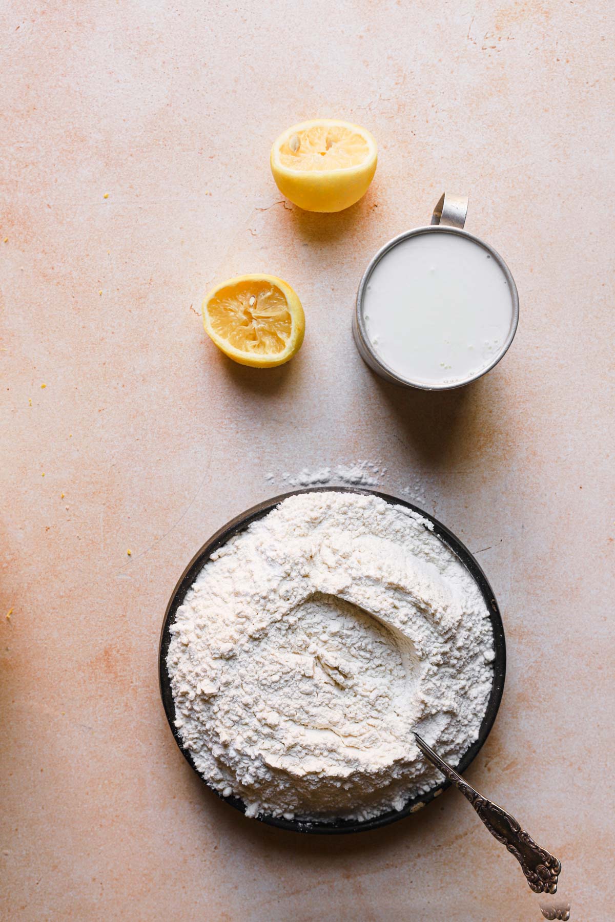 Two lemon halves, a cup with milk and a bowl with flour mixture.