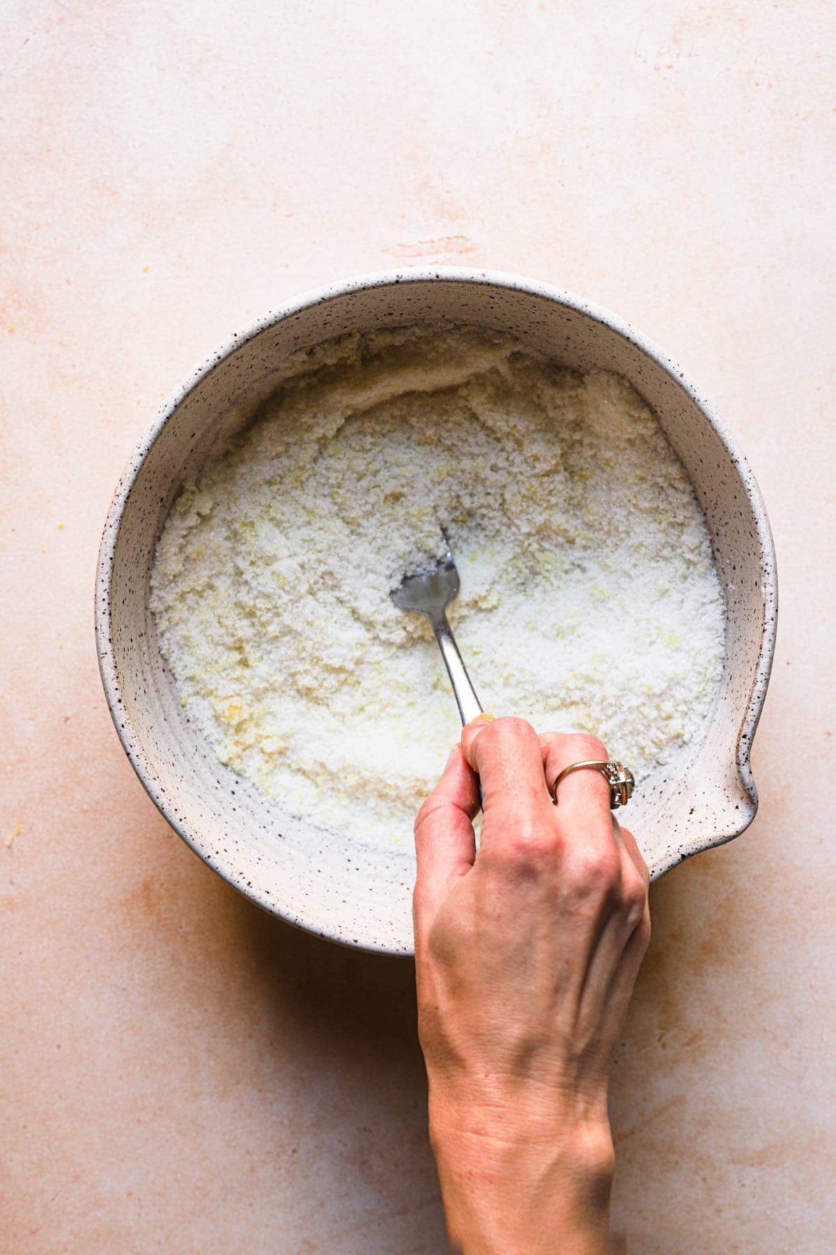 A hand mixing lemon zest with sugar.