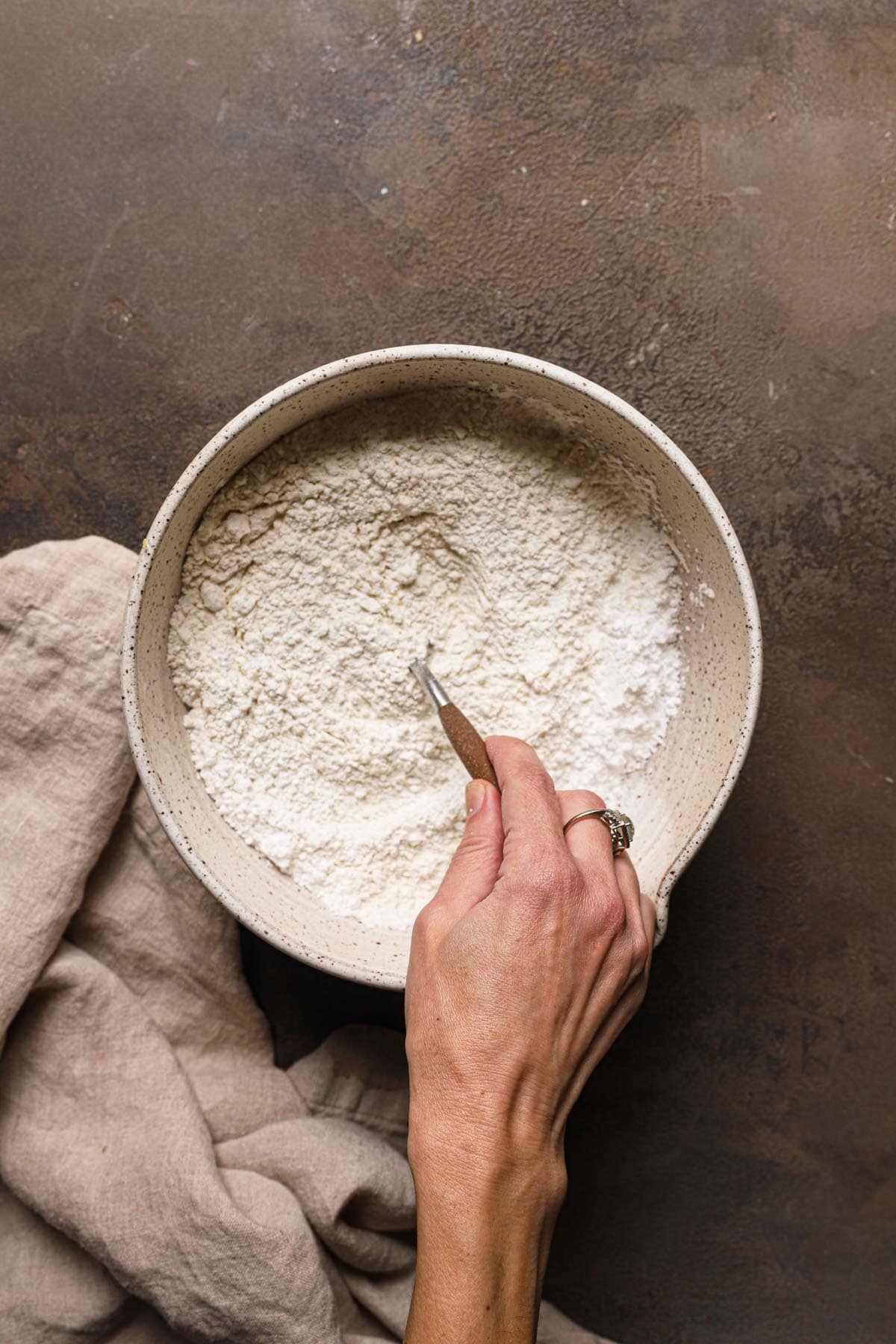A hand mixing flour in a large bowl.