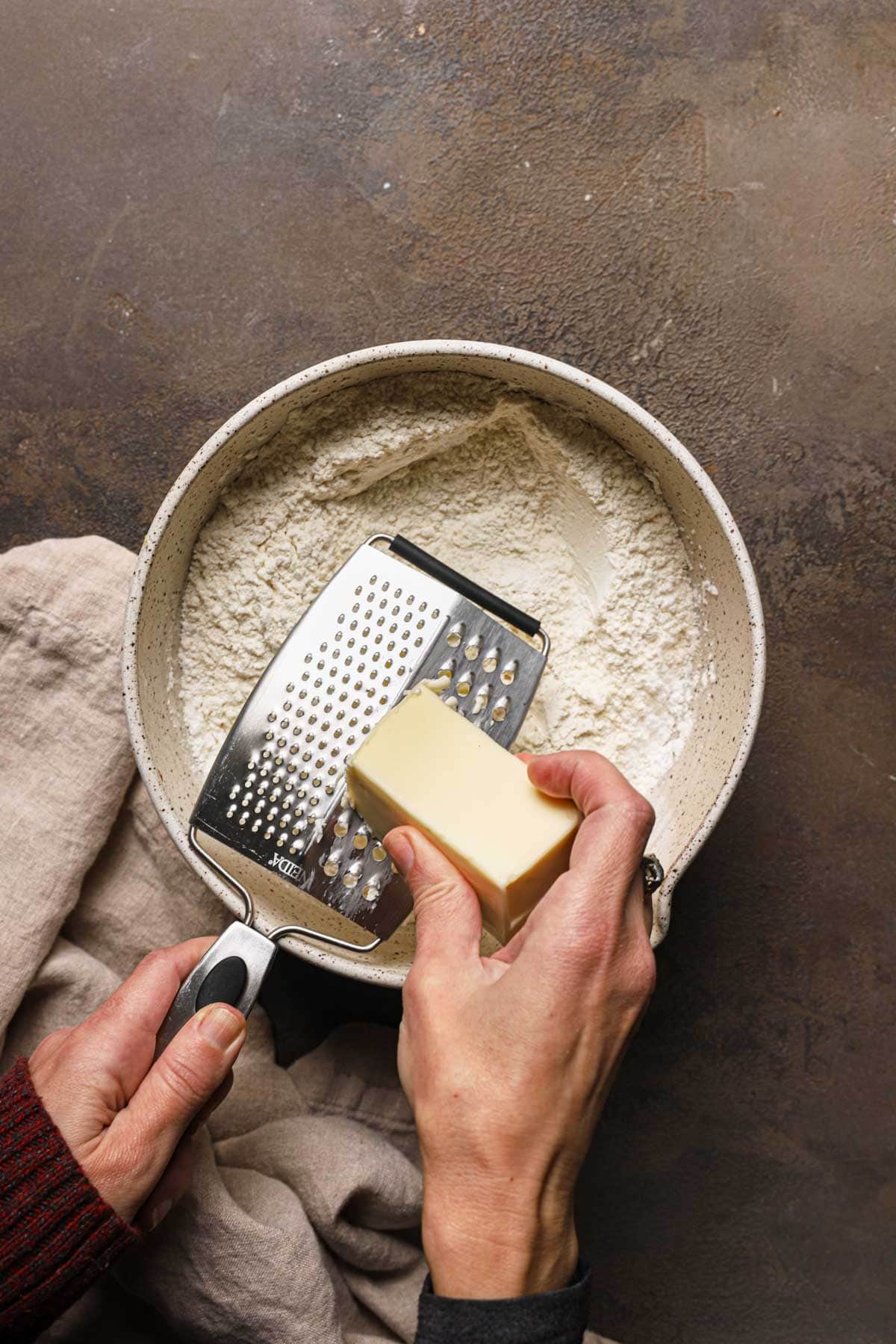 A hand grating butter into a large bowl with flour.