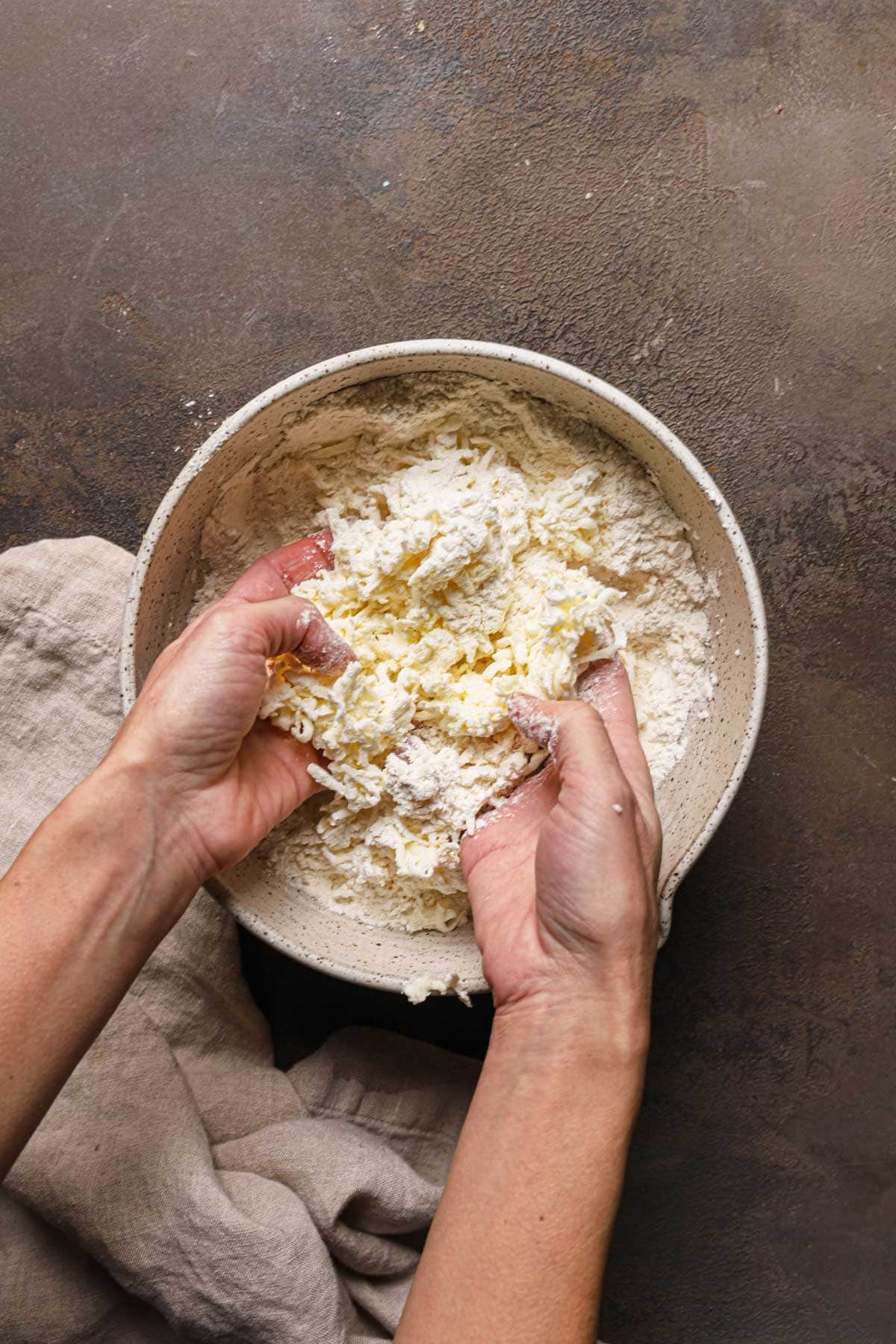 Hands rubbing butter into flour in a large bowl.