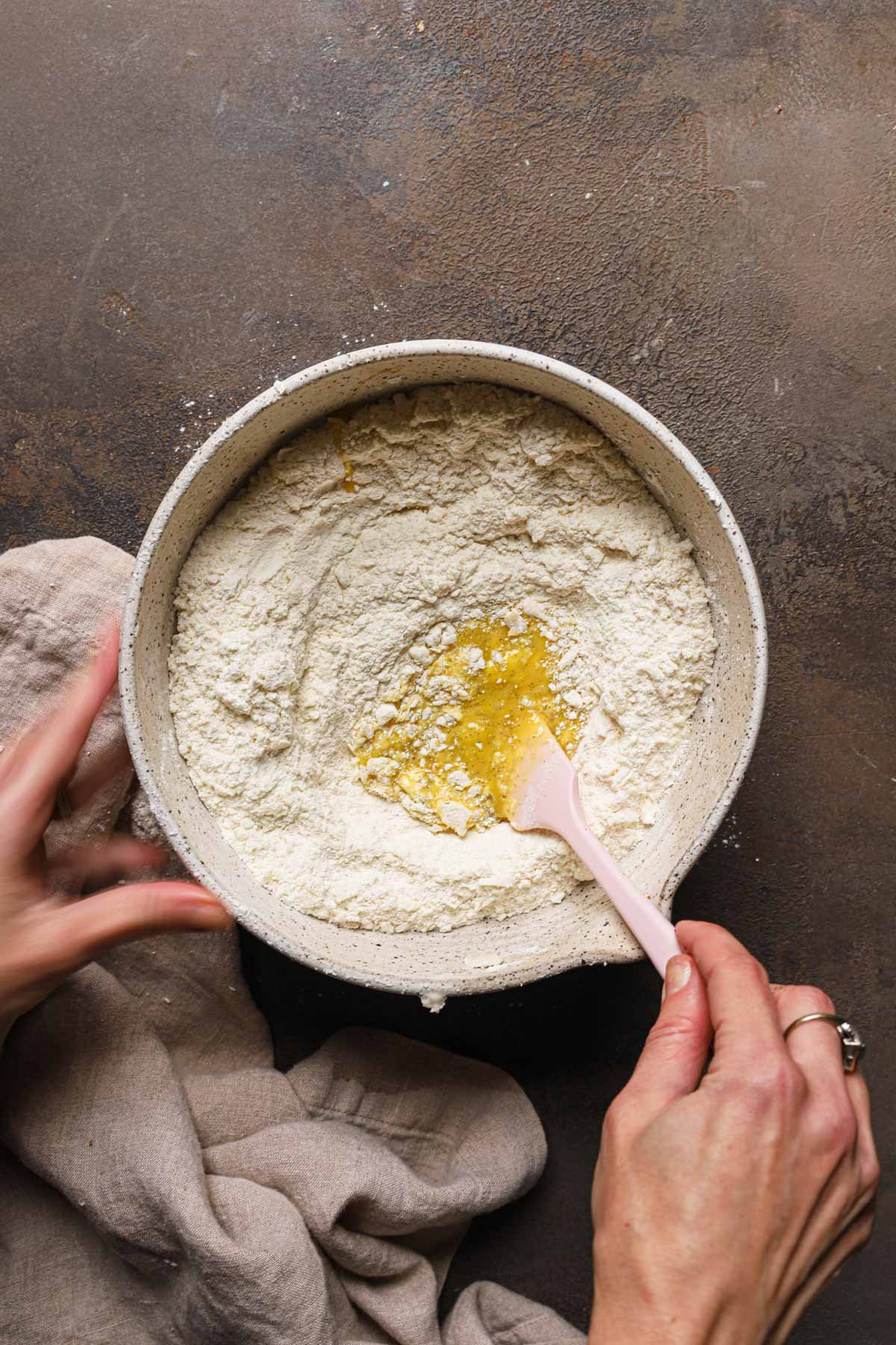 Hands mixing eggs into a large bowl with flour.