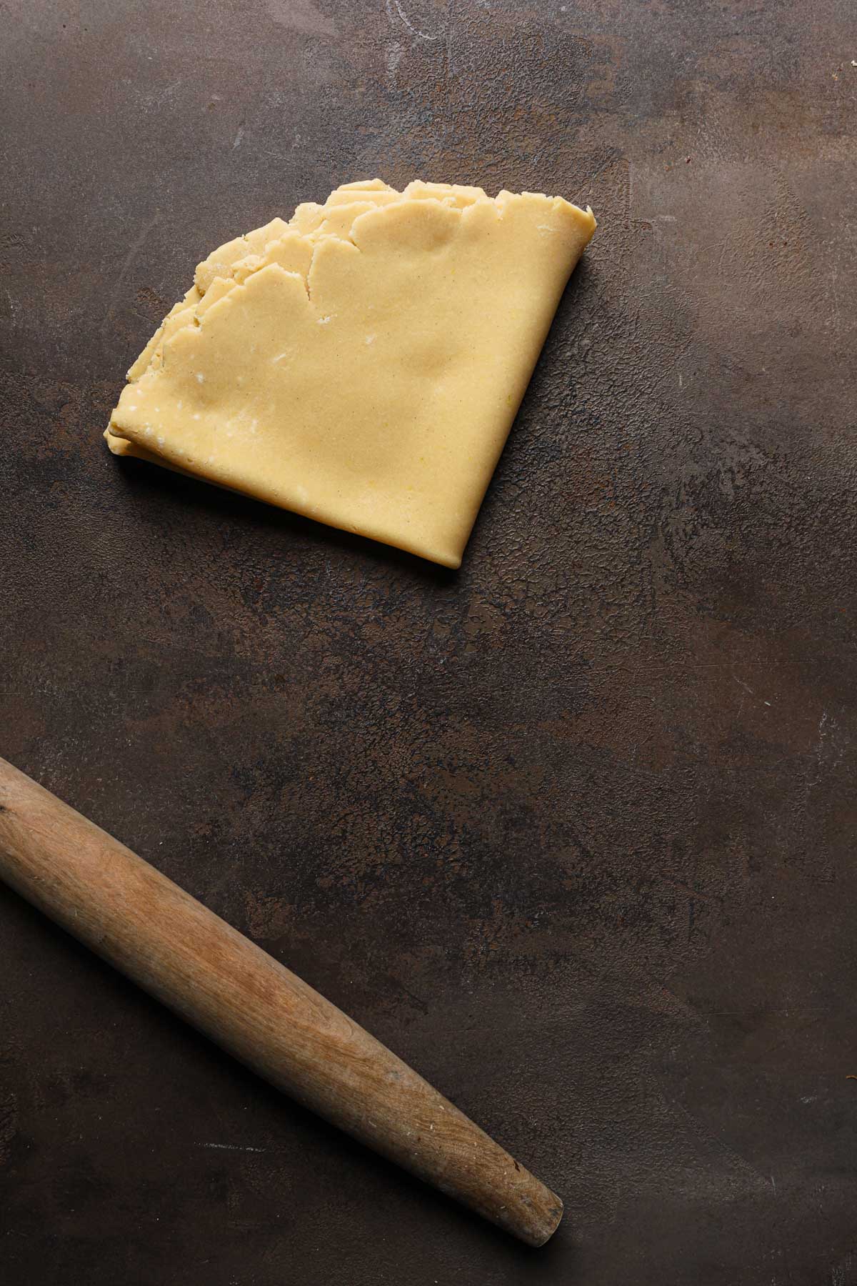 Rolled dough folded over itself in a triangle shape next to a rolling pin.