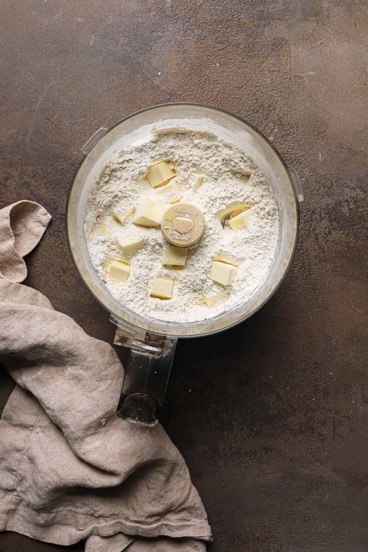 A food processor bowl with flour and pieces of butter.