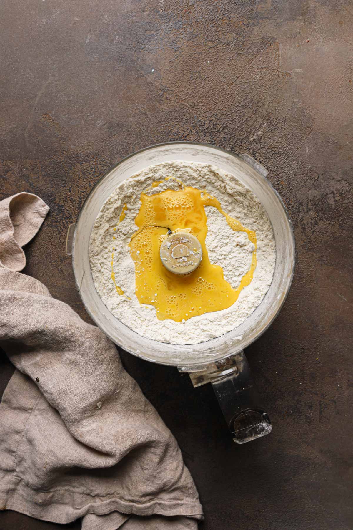 A bowl of a food processor with flour and beaten egg.