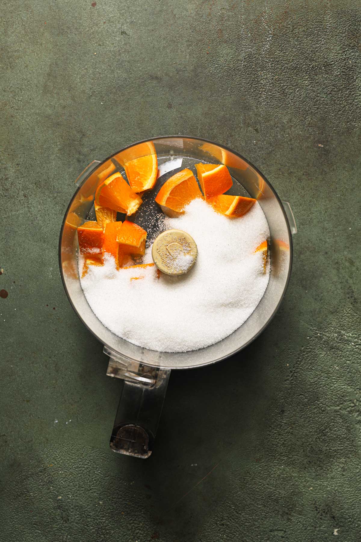 A food processor bowl with fresh orange pieces and sugar.