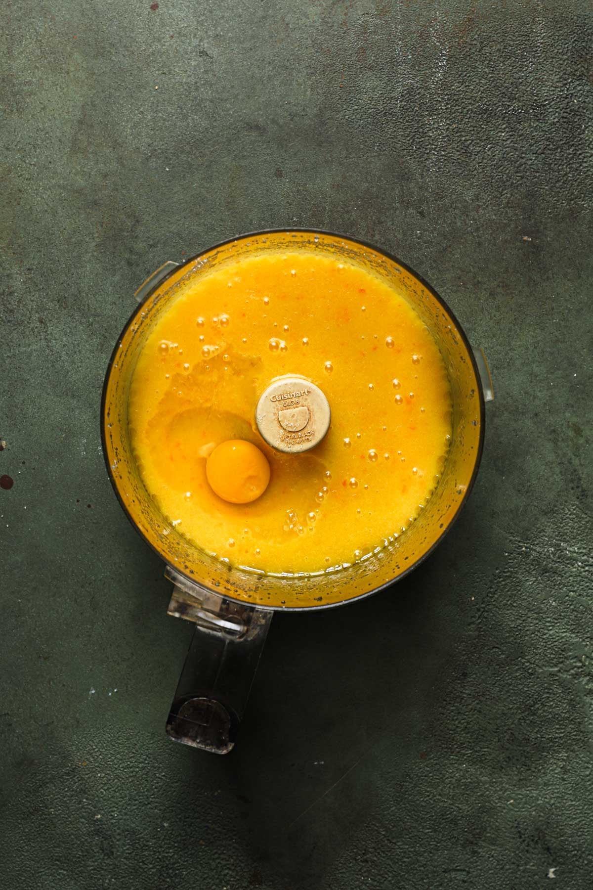 A food processor bowl with pureed fresh orange and an egg.