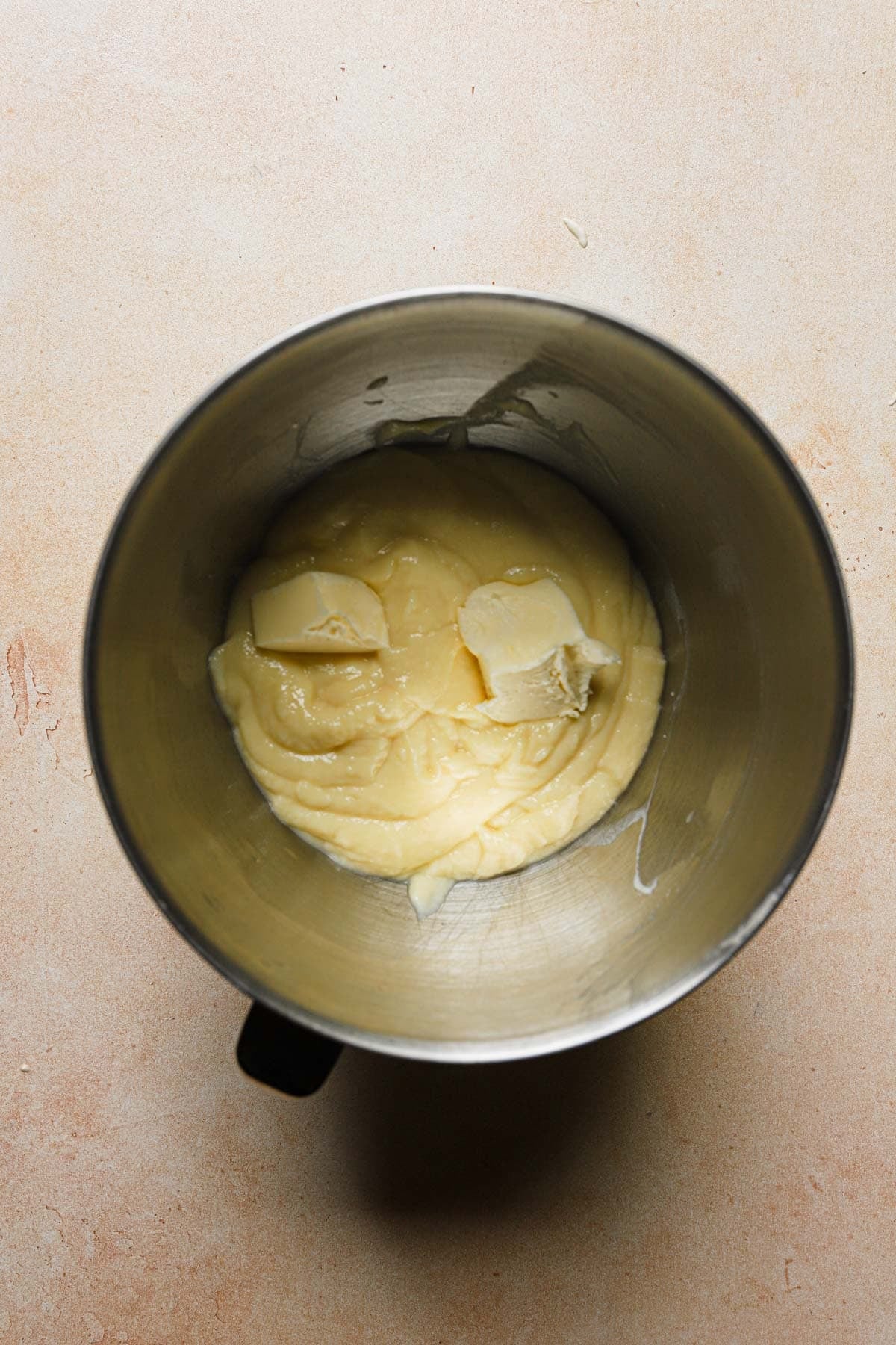 A pastry cream in a mixing bowl and pieces of butter.