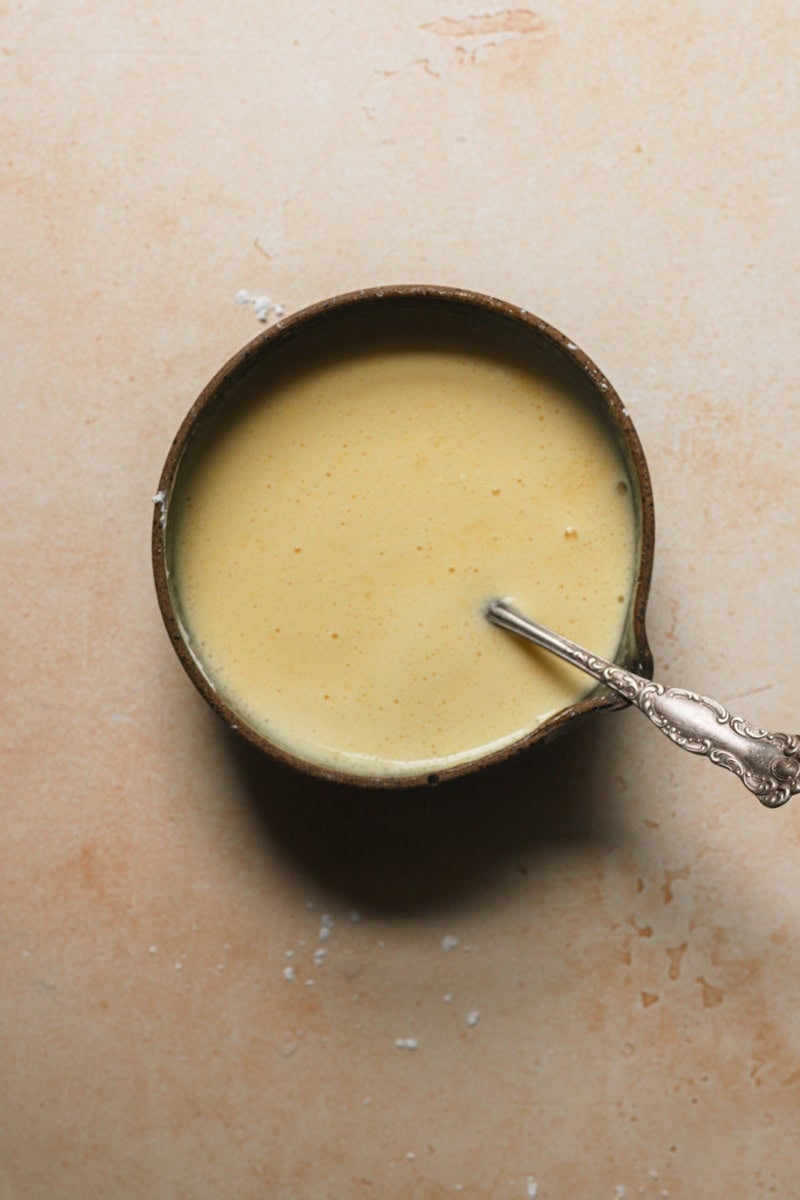 A bowl with egg yolk and milk mixture with a fork.