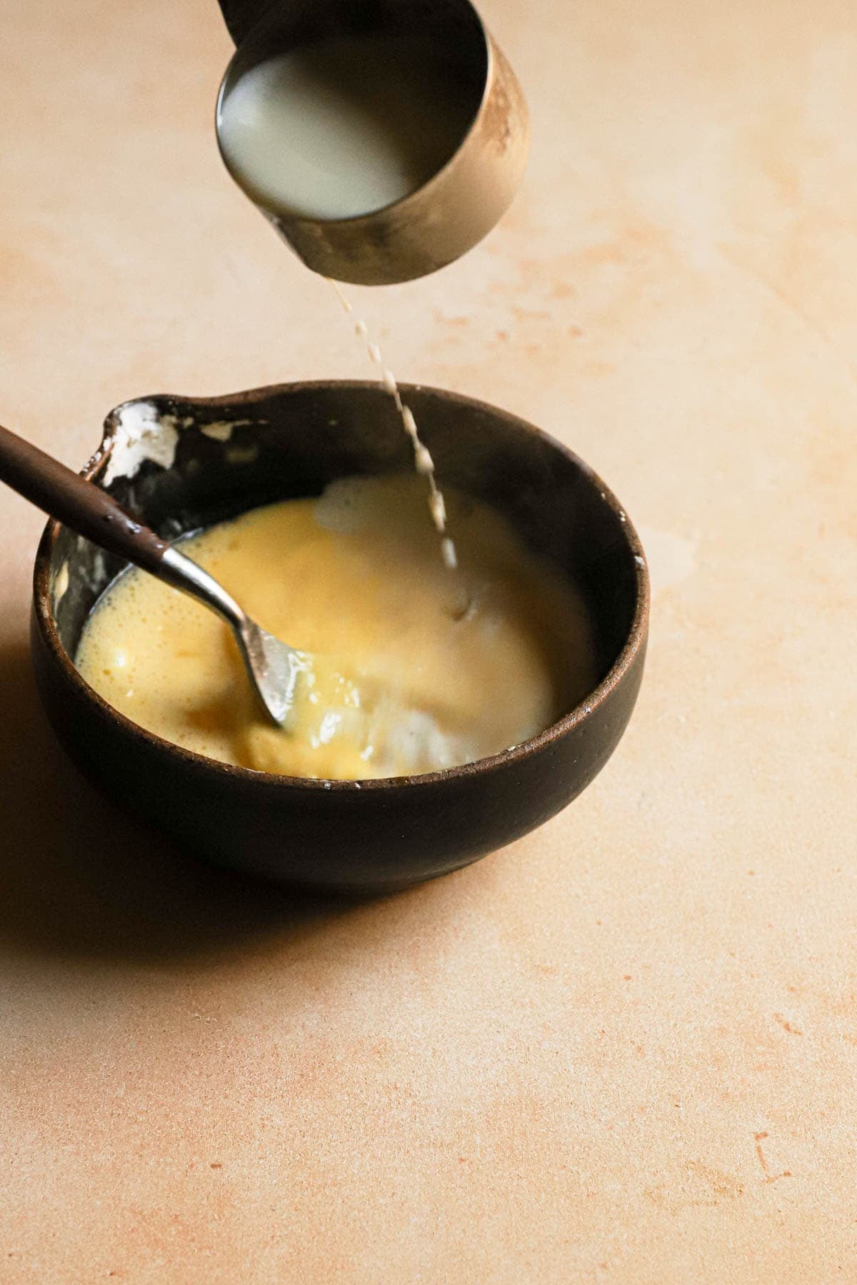 Pouring milk into the egg yolk mixture while stirring.