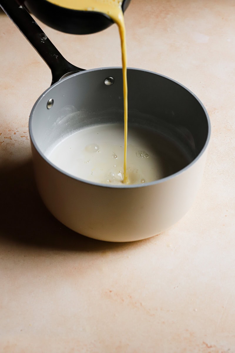 Pouring egg yolk mixture into a pan with milk.