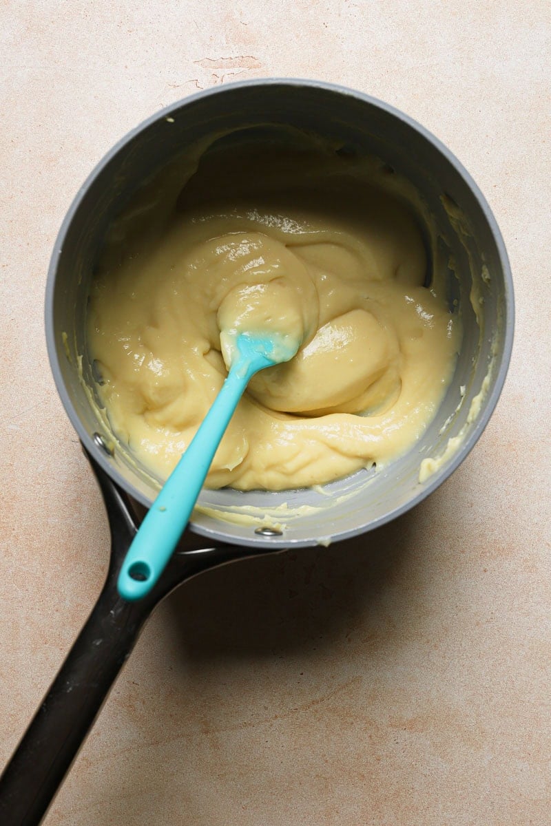 A thickens pastry cream in a pan with a spatula.