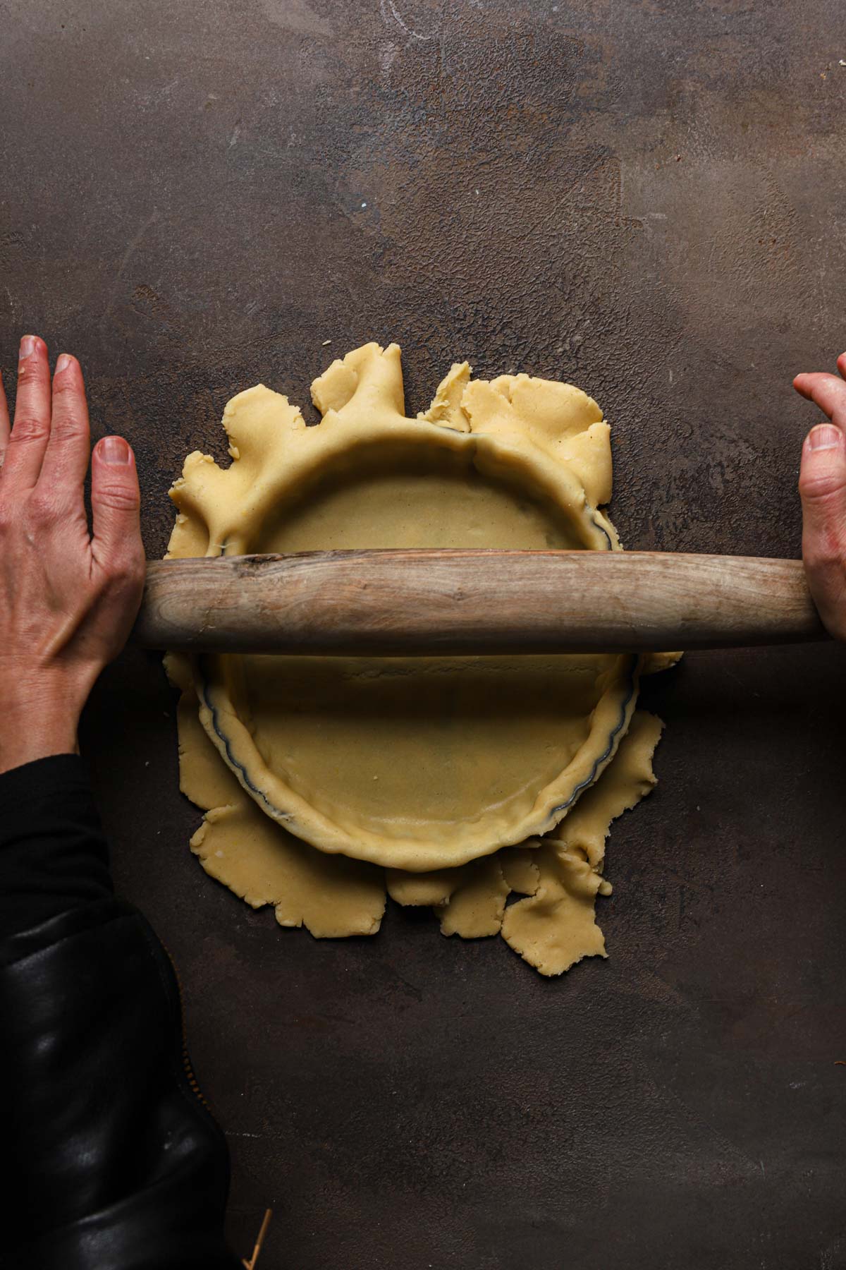 Hands rolling over a tart pan.