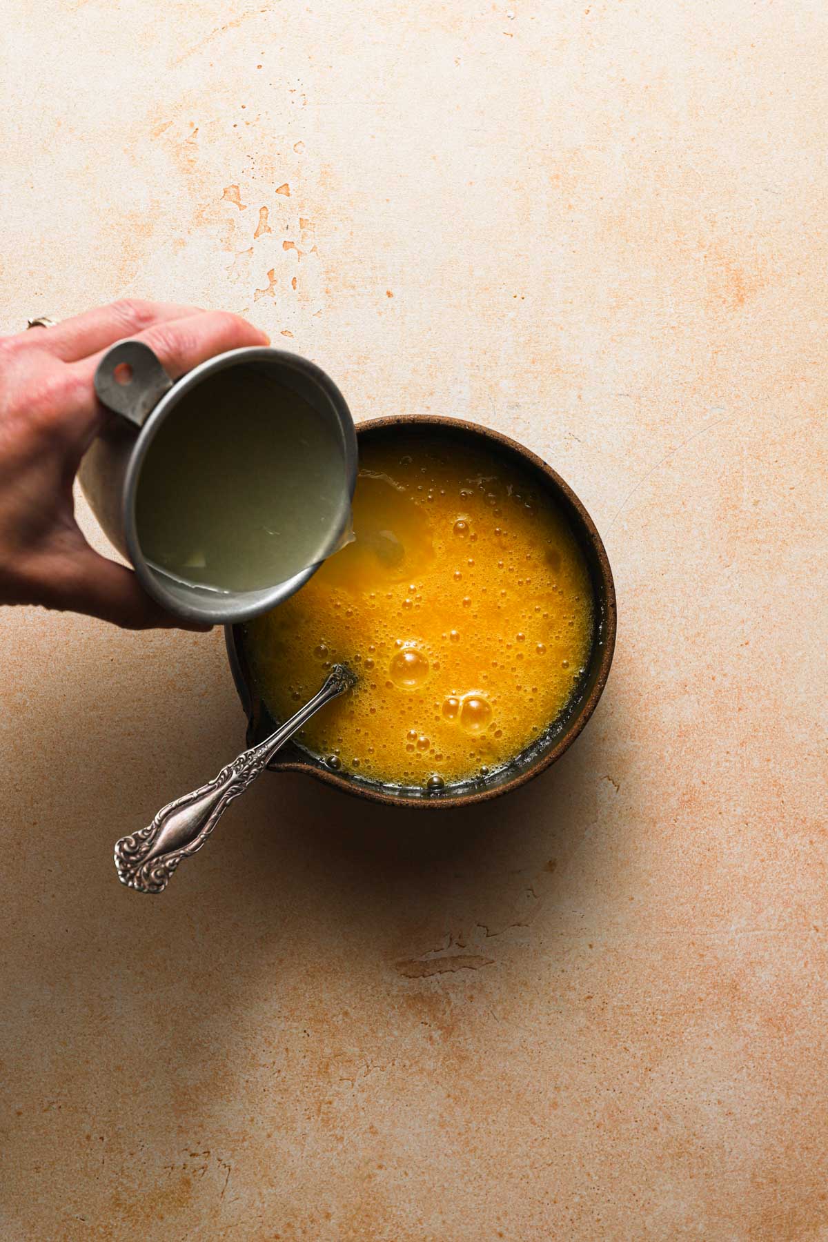 Pouring lemon juice into a bowl with egg mixture.