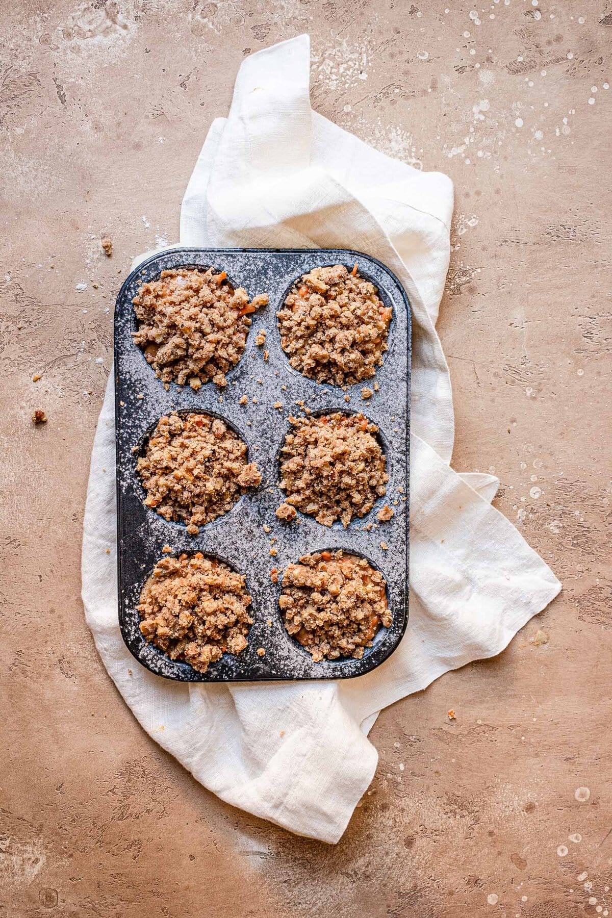 A muffin tin filled with muffin batter topped with streusel.