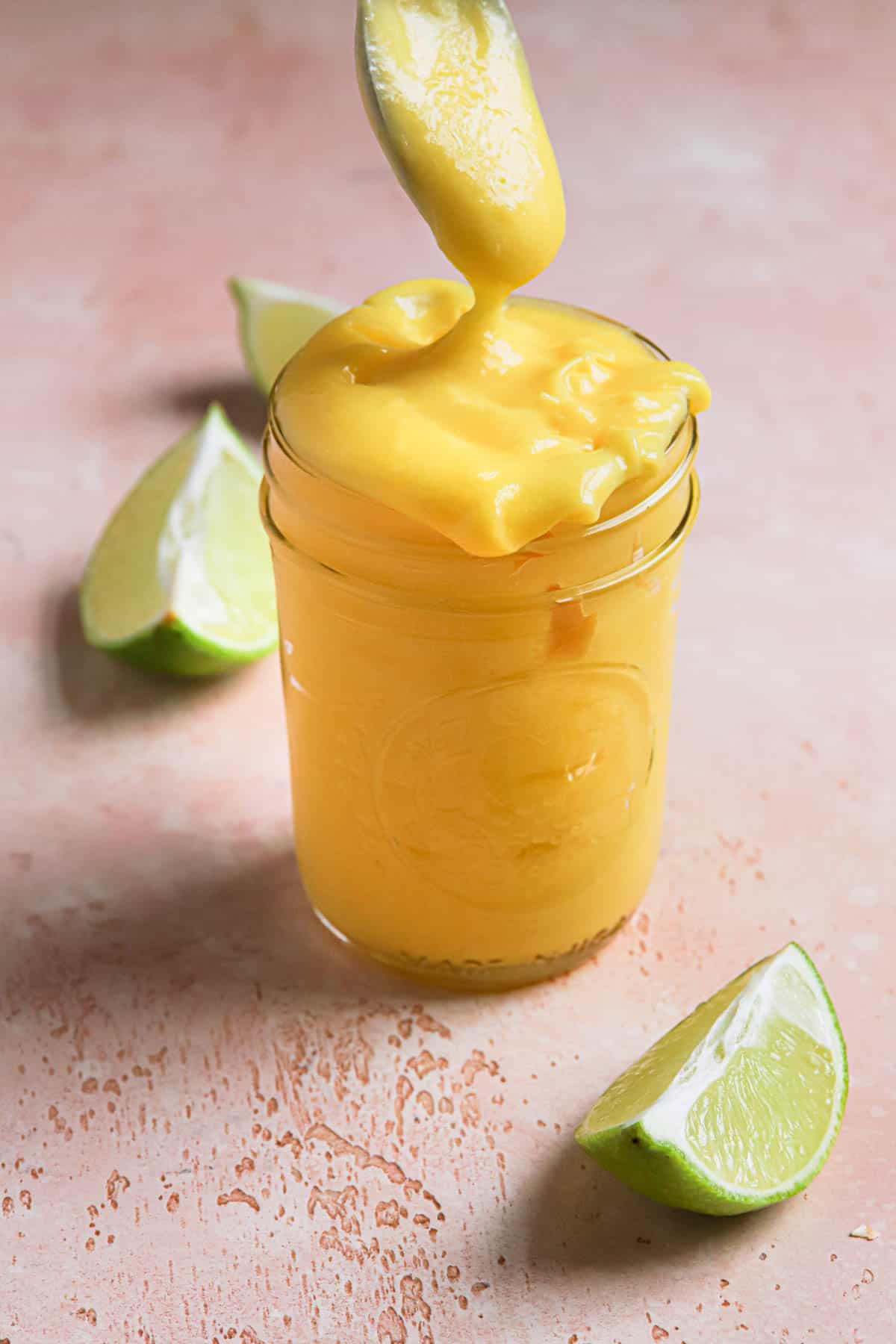 a glass jar filled with curd, limes around it and spoon dipping.