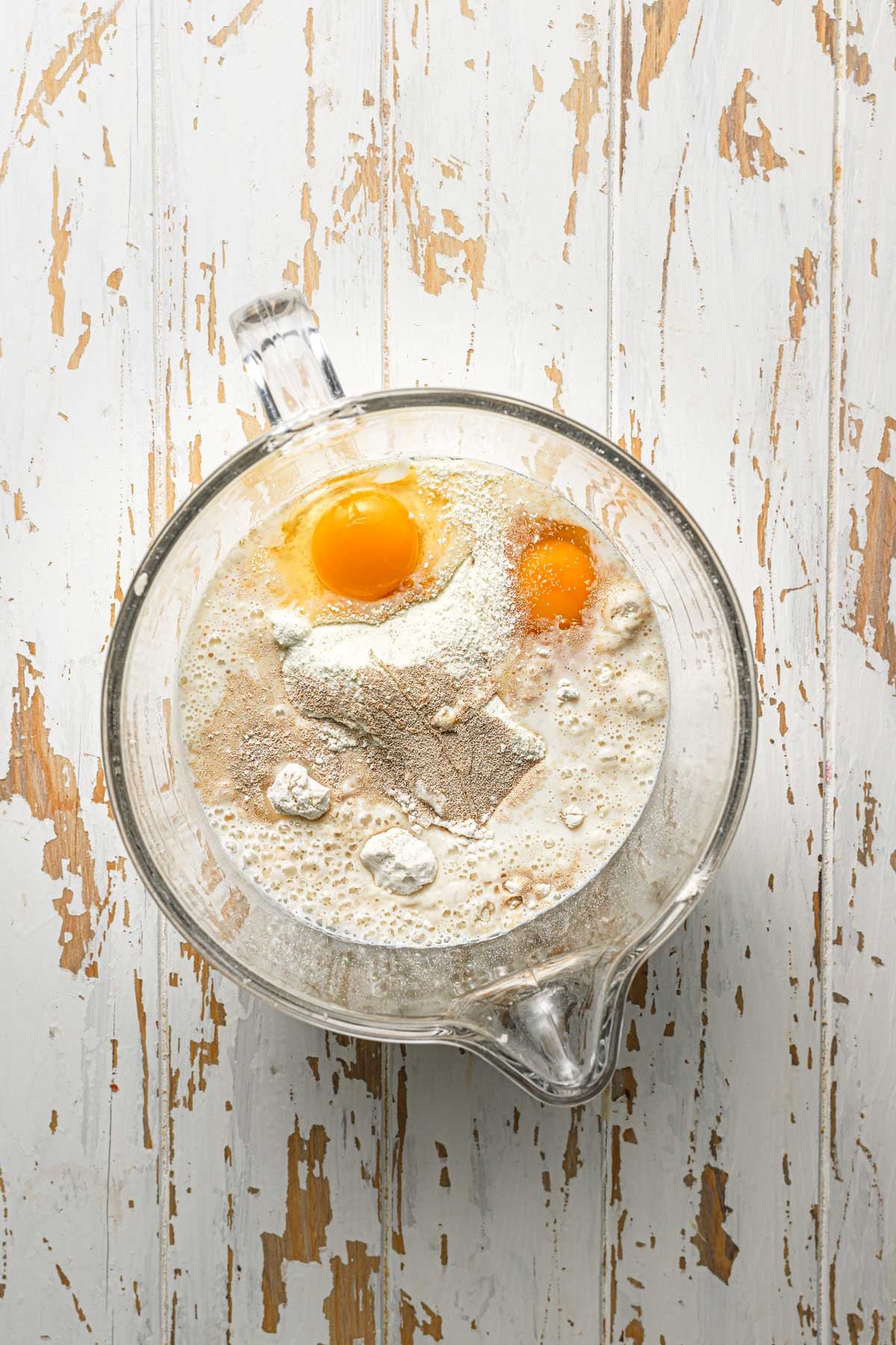 A mixer bowl with flour, eggs, yeast and milk.