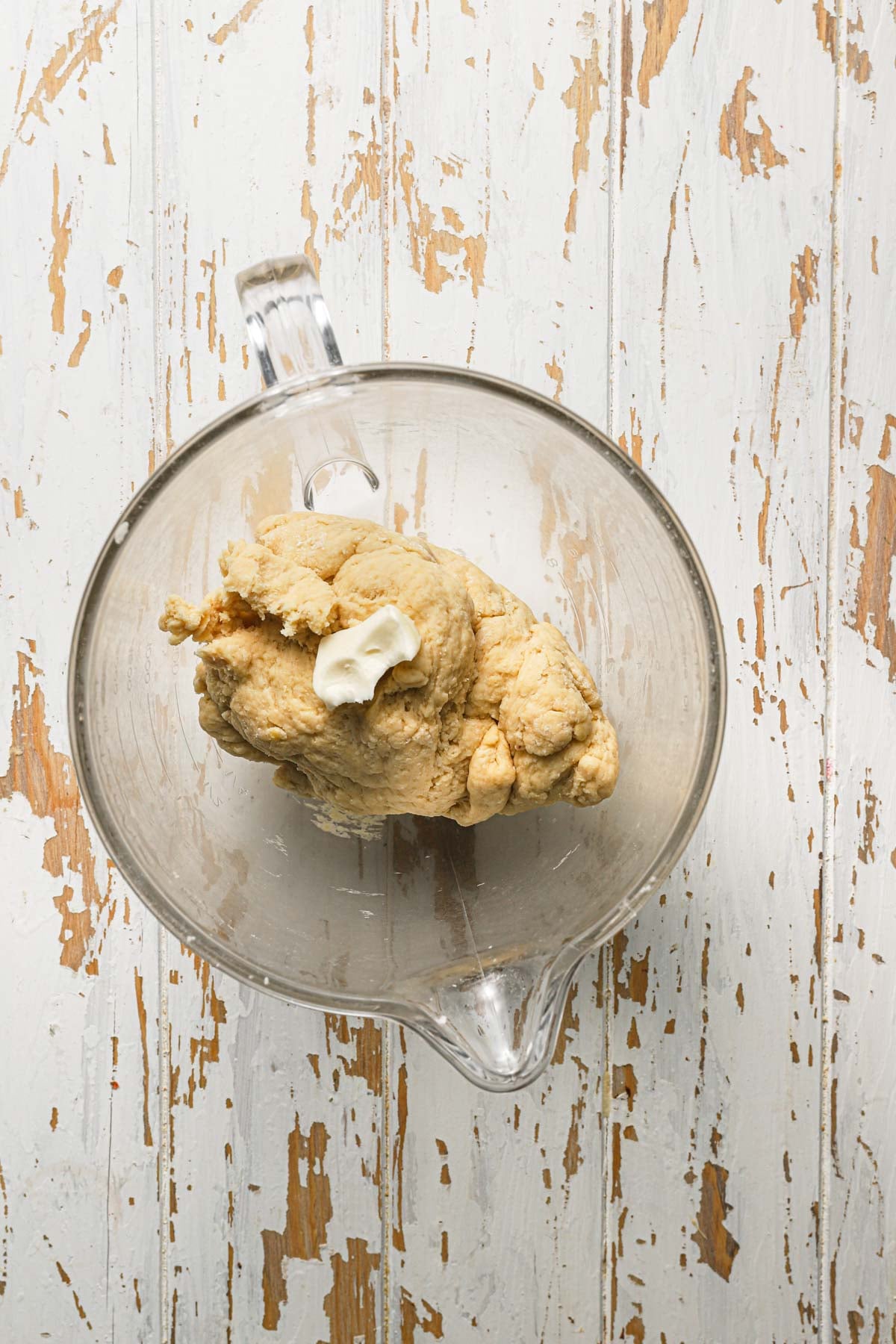 A mixer bowl with dough and apiece of butter.