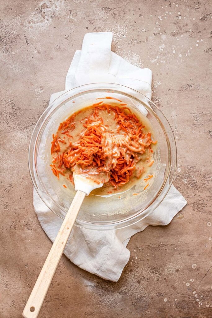 A large bowl with egg mixture and shredded carrots.