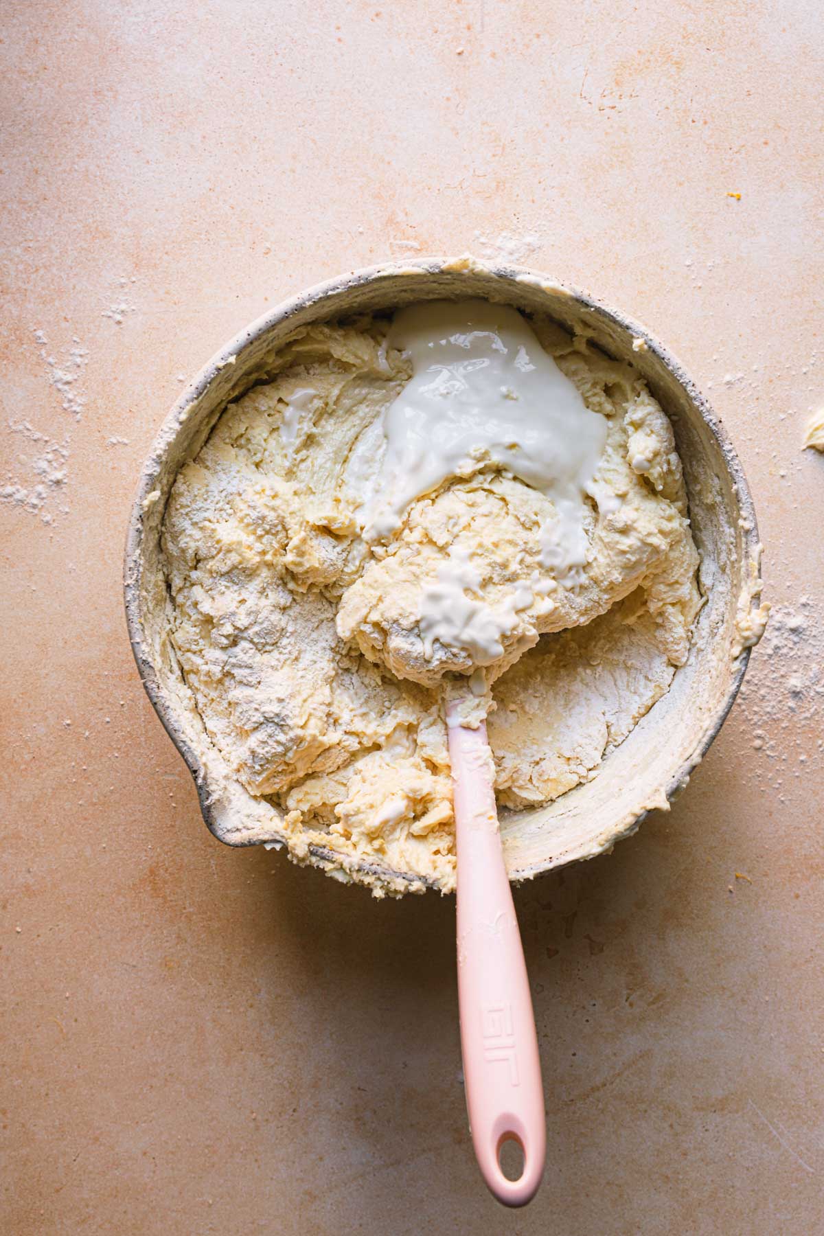 A bowl with cake batter with flour and a spatula.