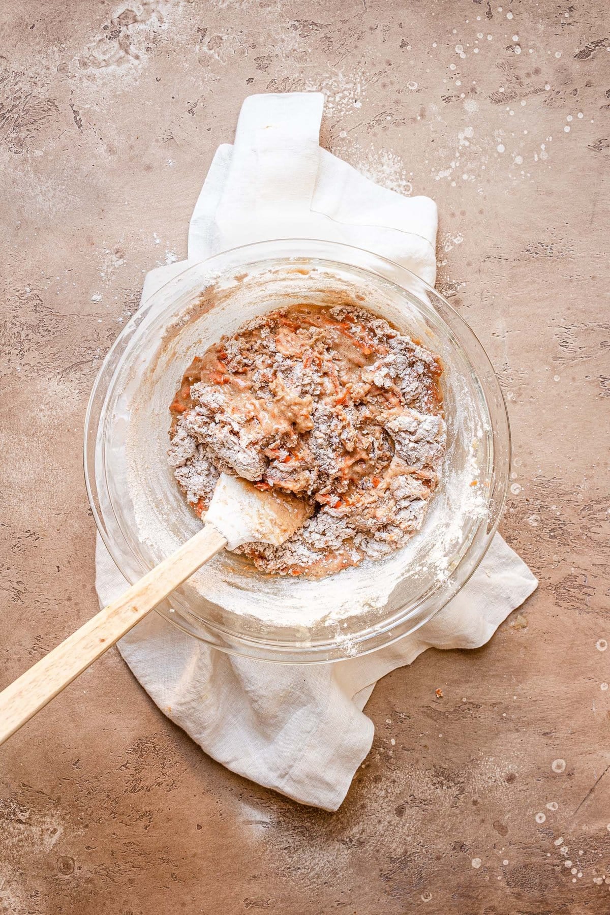 A spatula mixing in dry ingredients into a carrot batter.