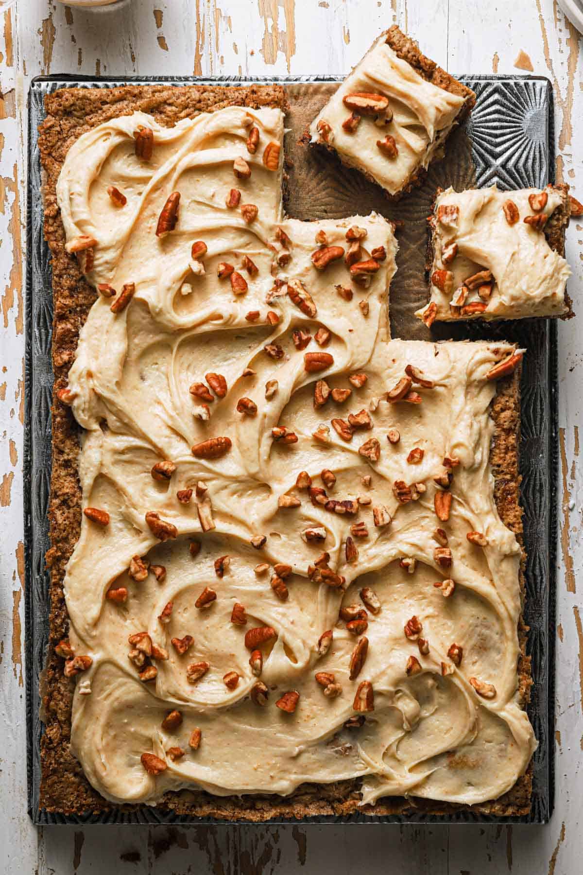 carrot sheet cake topped with frosting and nuts over a pan.