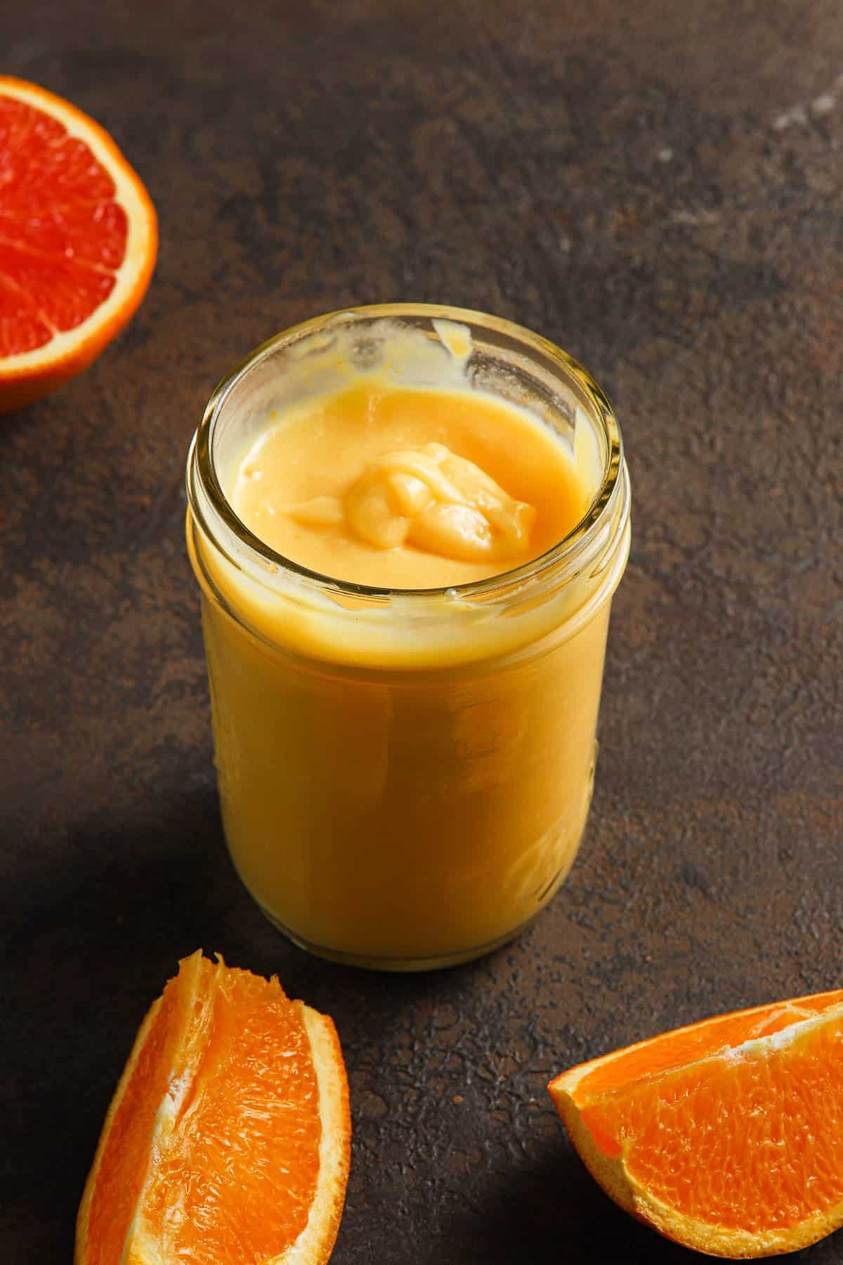 orange curd in a jar with slices oranges around.