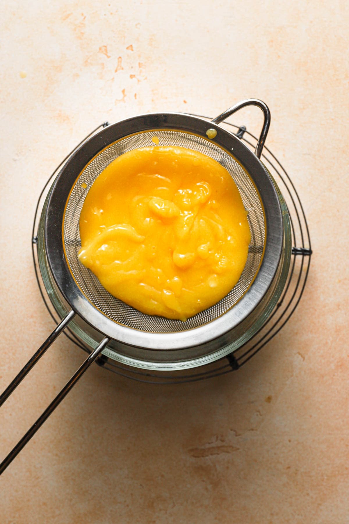 Lemon curd over in a sieve over a bowl. 