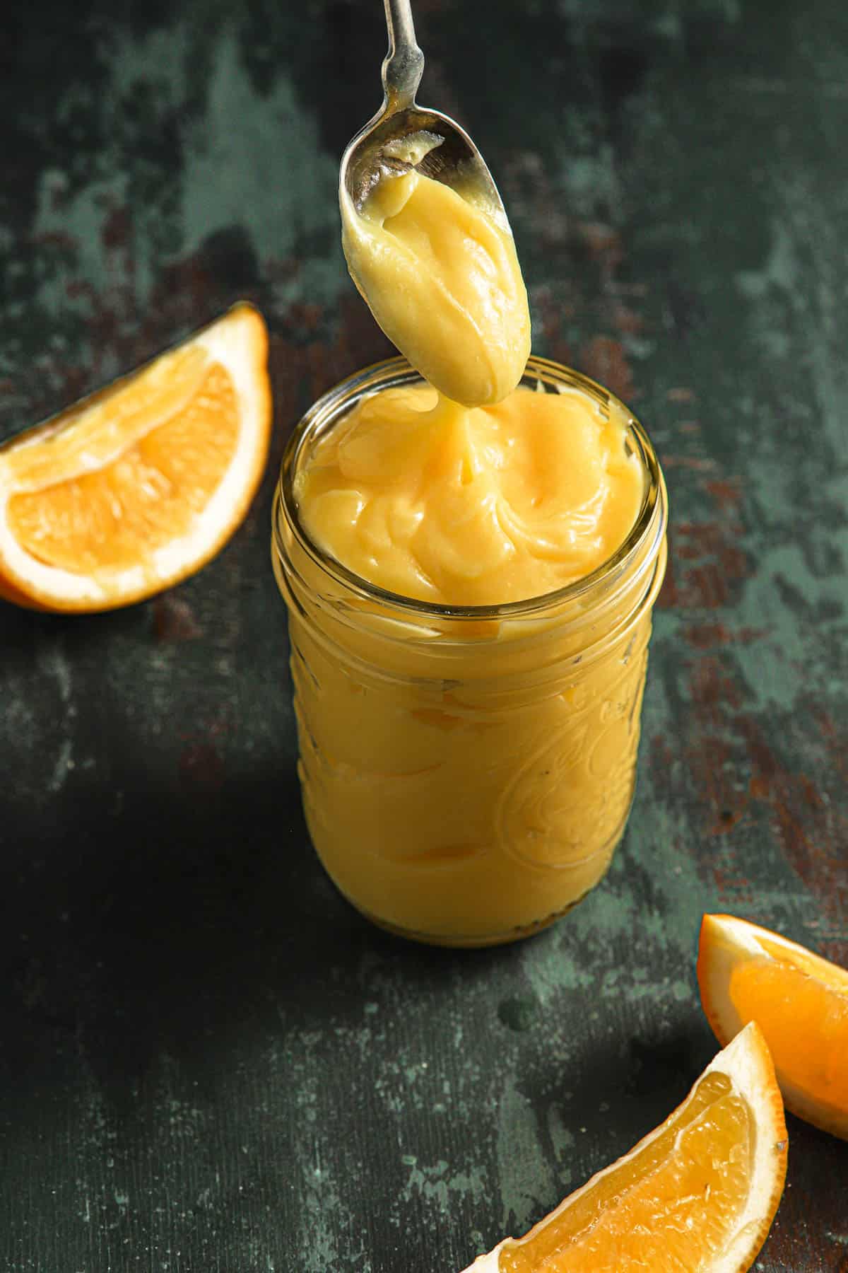 Meyer lemon curd in a glass jar with a spoon.