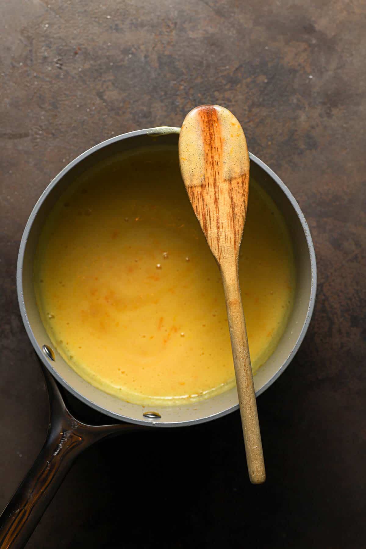 Thickened orange custard in a saucepan with a spoon.