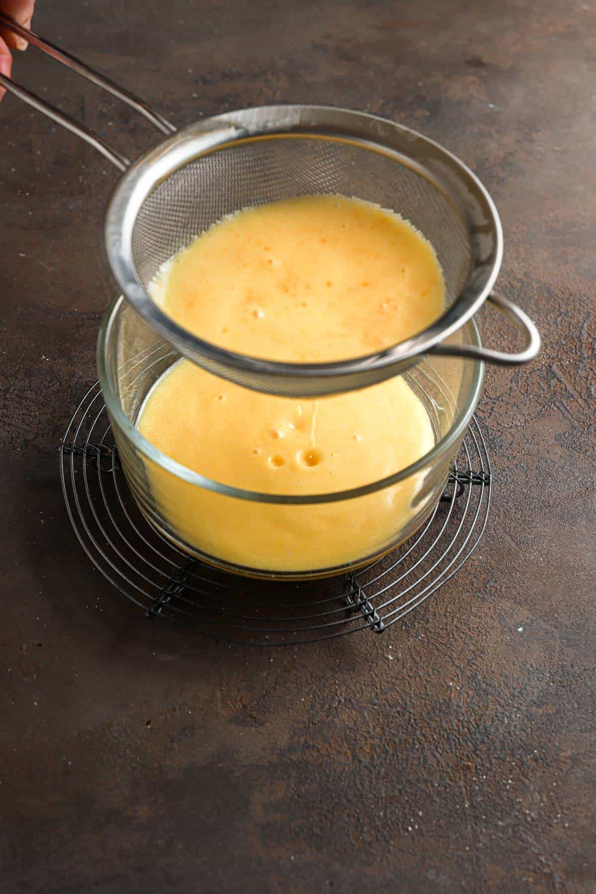 Straining citrus curd through a sieve into a bowl.