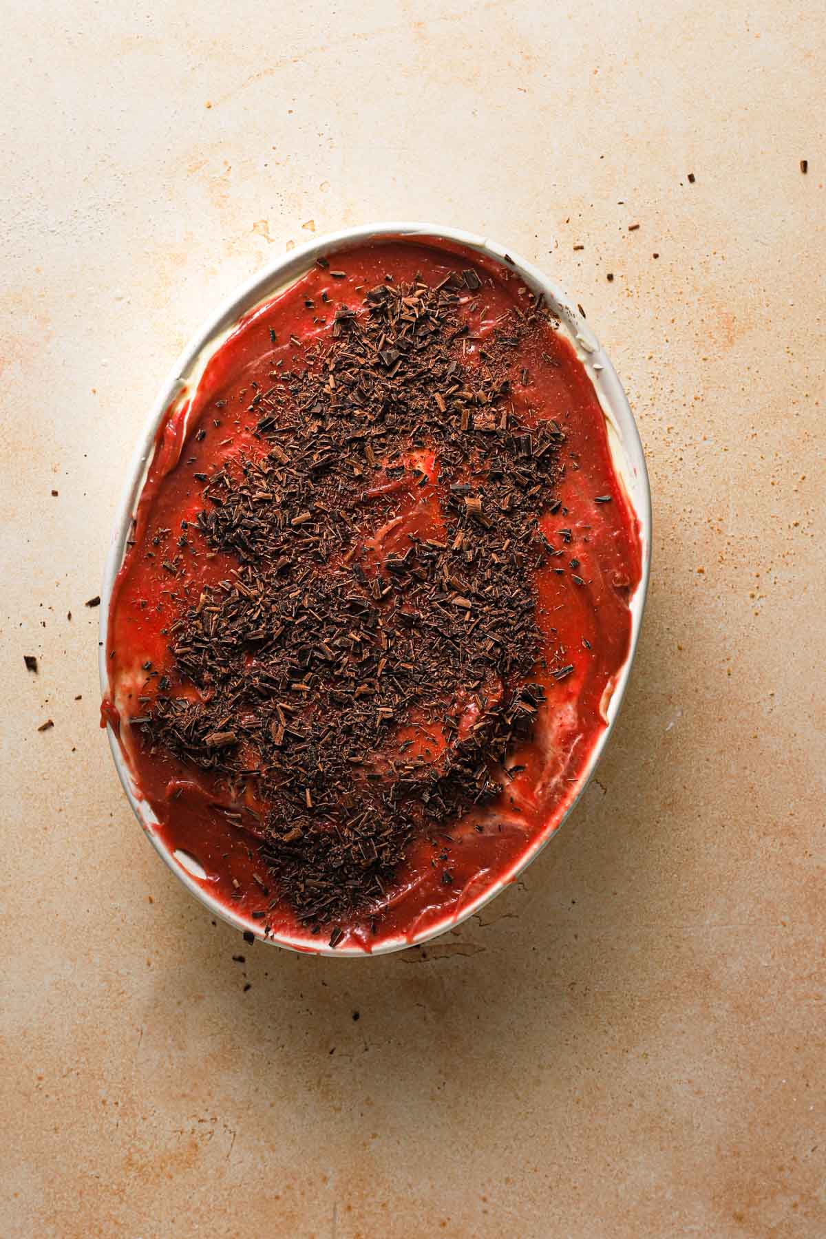 A dish with a layer of raspberry curd and chopped chocolate.