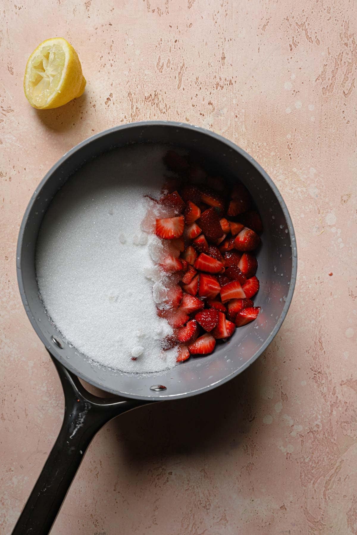 A sauce pan with sugar, chopped strawberries and squeezes lemon.
