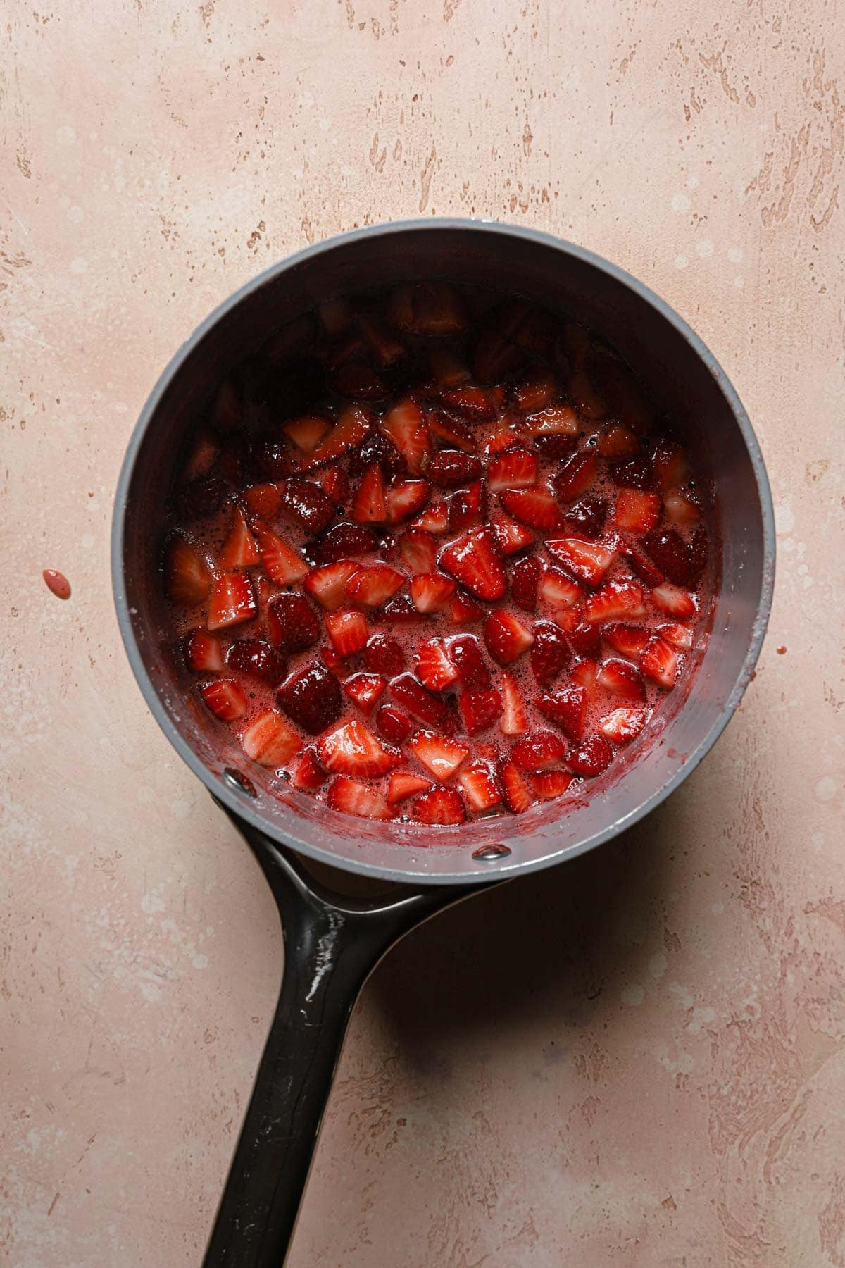 A sauce pan with chopped strawberries in syrup.