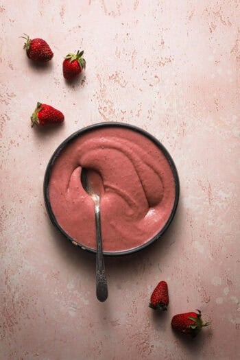 a bowl with a pink custard and strawberries around it.