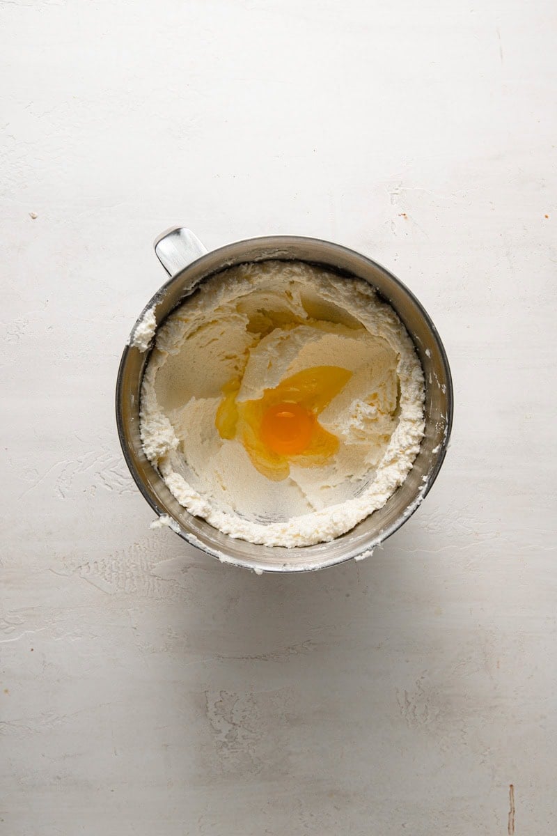 A bowl of a stand mixer with whipped butter and an egg.